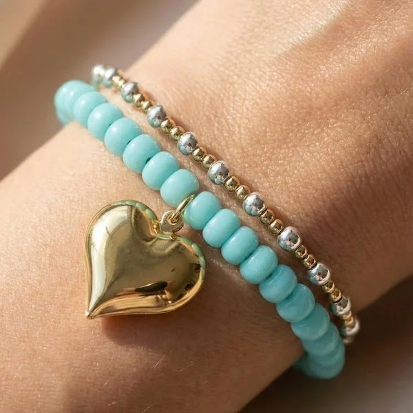 robin egg blue czech glass puffy heart bracelet on a wrist within a mixed-metal bracelet stack.