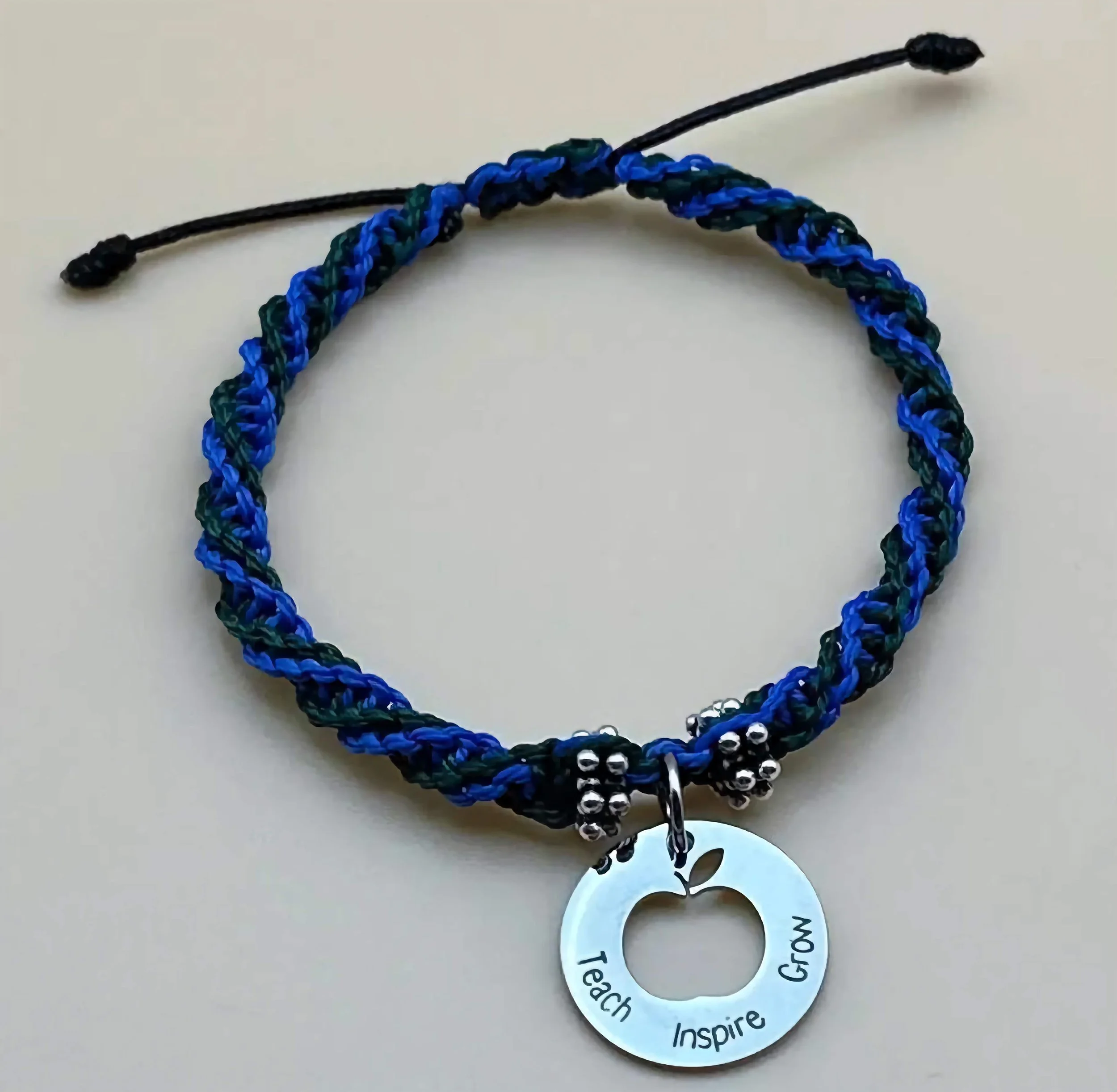 A close-up of a handmade teacher appreciation bracelet featuring a 'teach inspire grow' engraved disc.