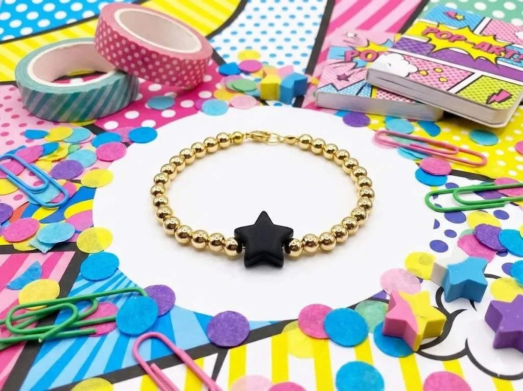 adjustable gold beaded bracelet with a customizable colorful silicone star charm on a neutral background.