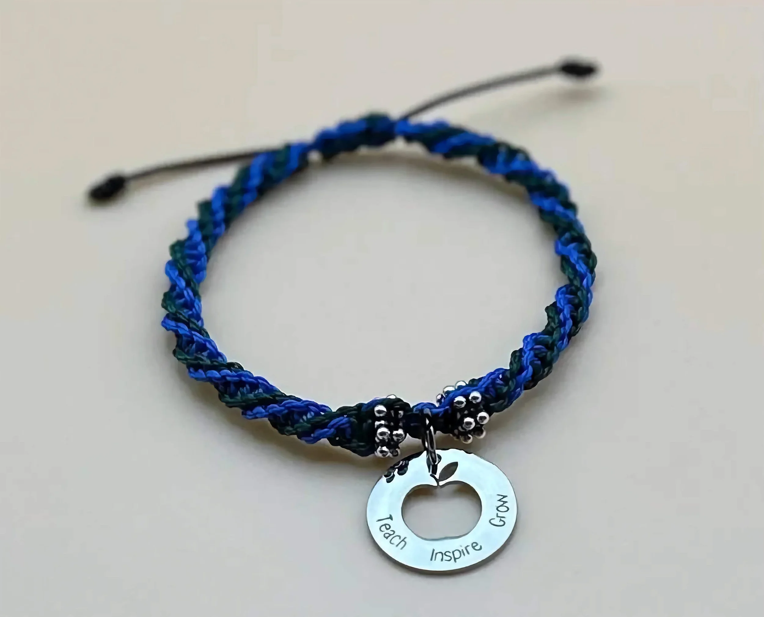 A close-up of a handmade teacher appreciation bracelet featuring a 'teach inspire grow' engraved disc.