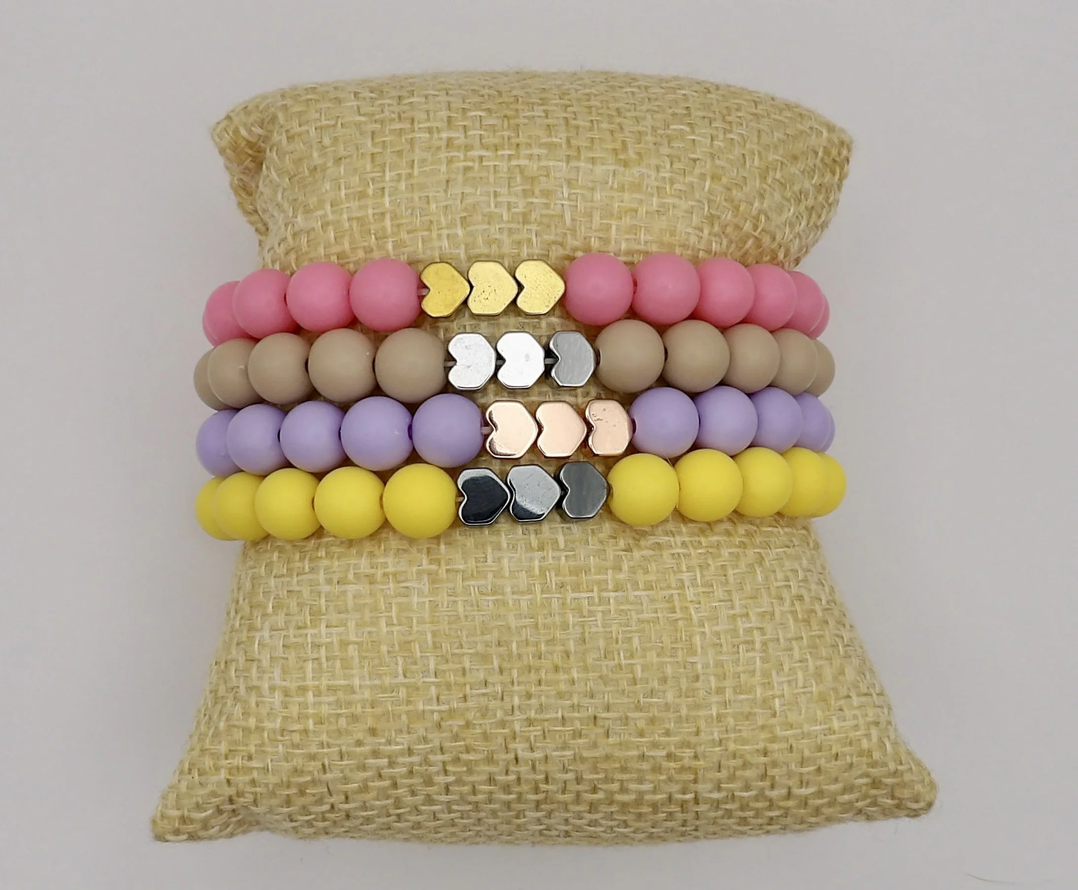 woman wearing a stack of dainty sweet dreams matte heart bracelets in soft pastel colors with metallic accents.