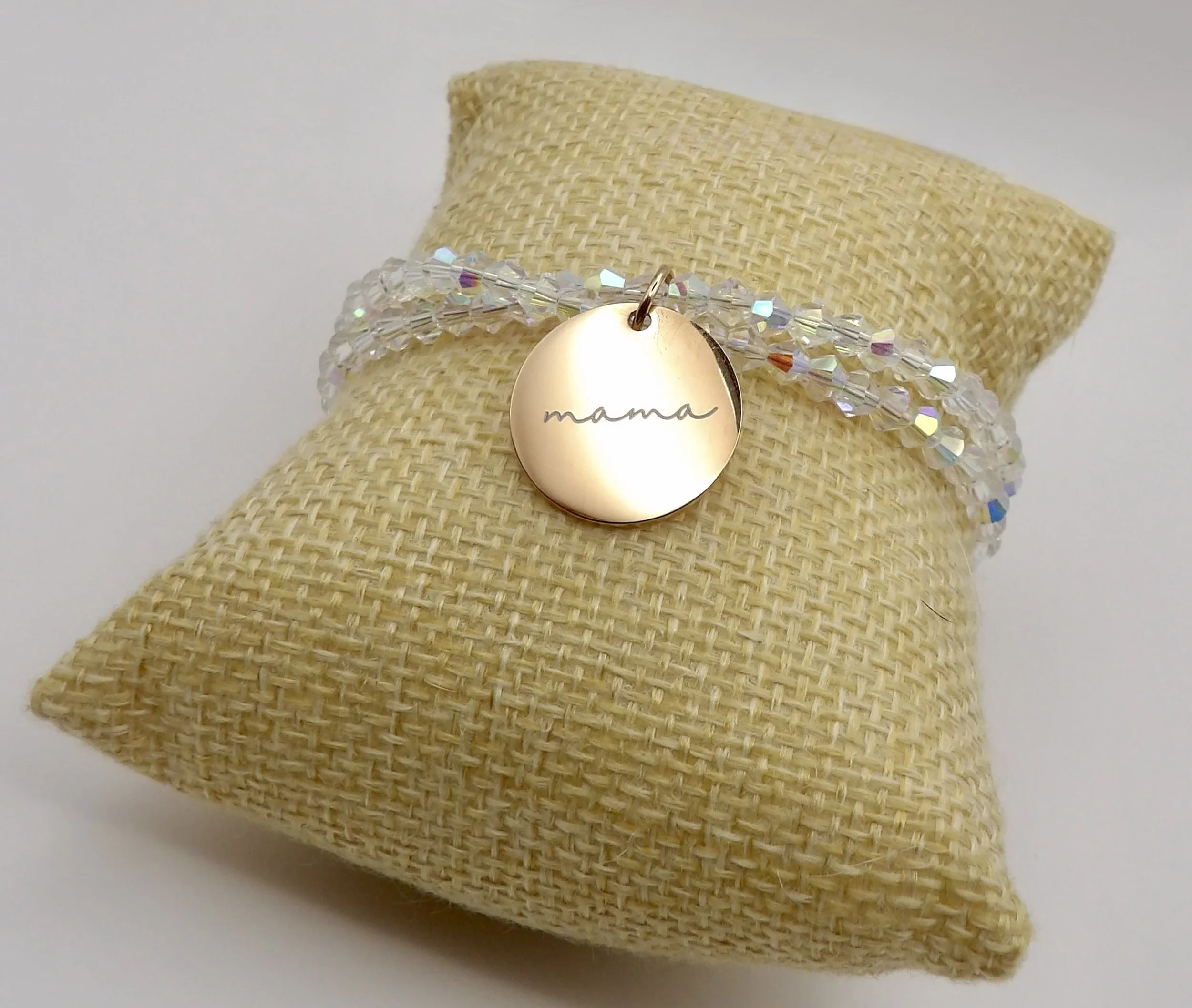 close-up detail of the 14k solid rose gold engraved "mama" disc charm on the crystal crossover bracelet.