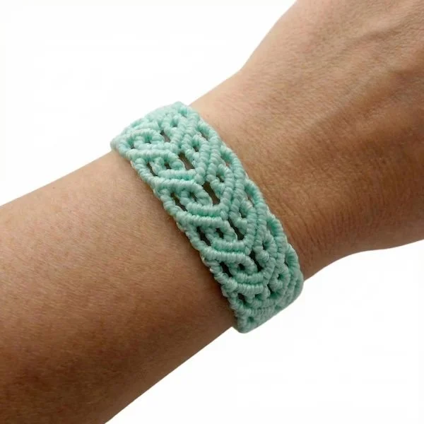 custom color micro-macramé celtic heart knot bracelet on a wrist with wood bead accents.