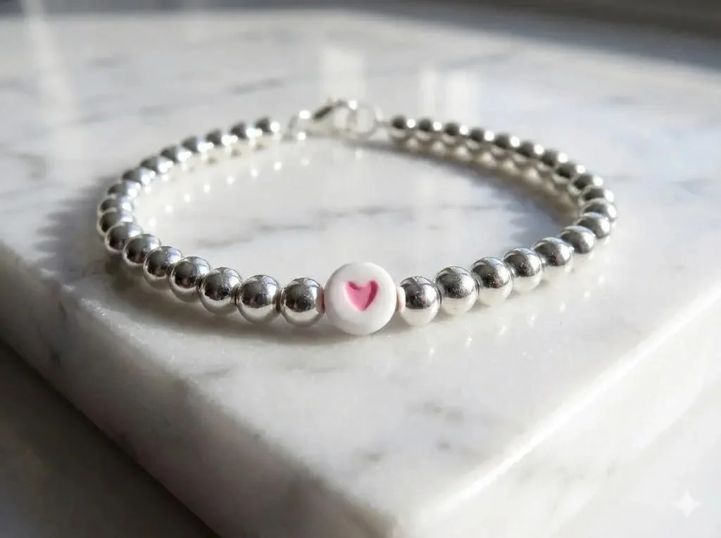 a minimalist sterling silver bead bracelet showing the polished silver surface and a vibrant, custom-colored heart pendant.