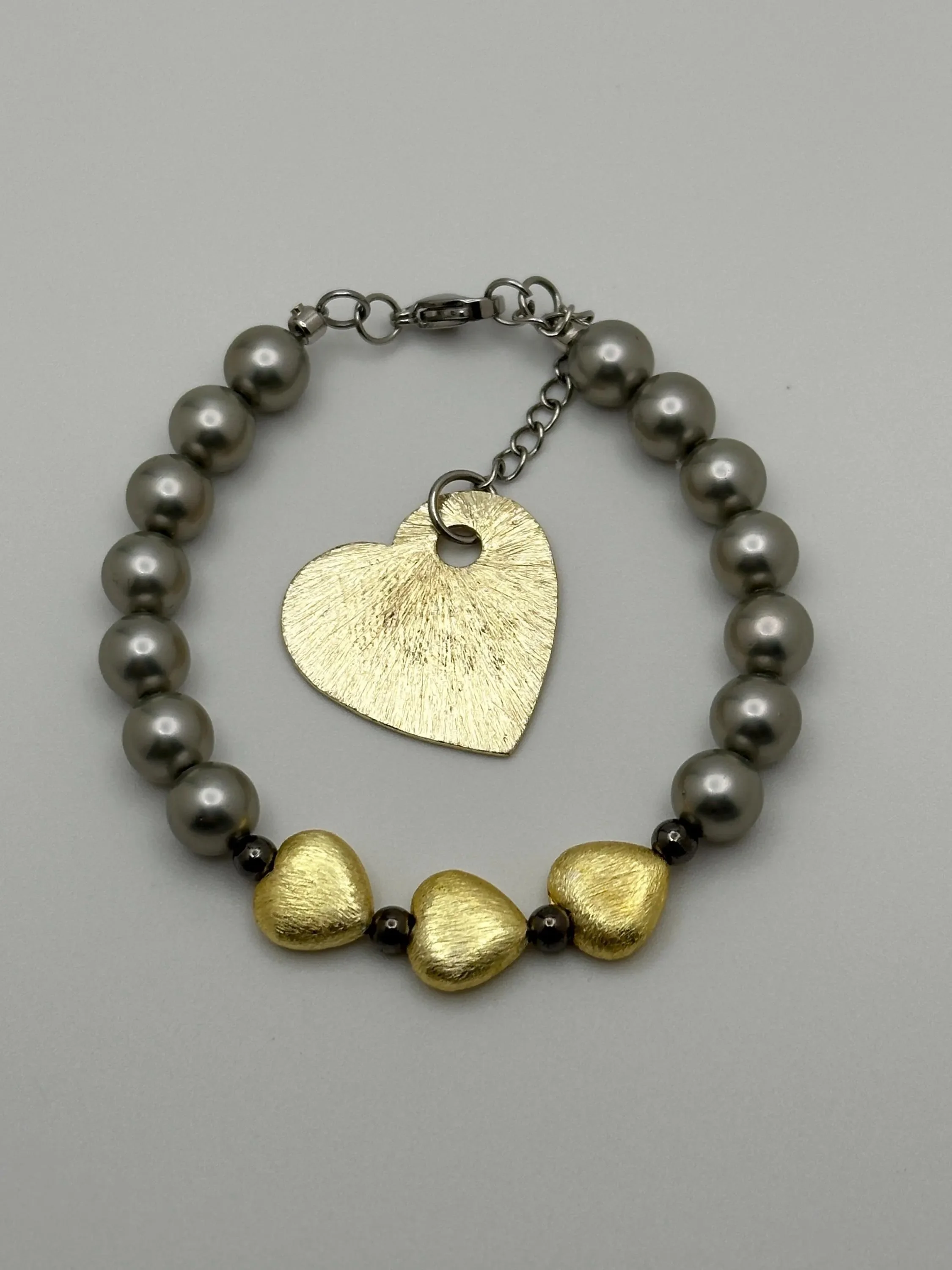 detailed view of the gunmetal mother of pearl textures and the soft matte finish of the gold heart charms.