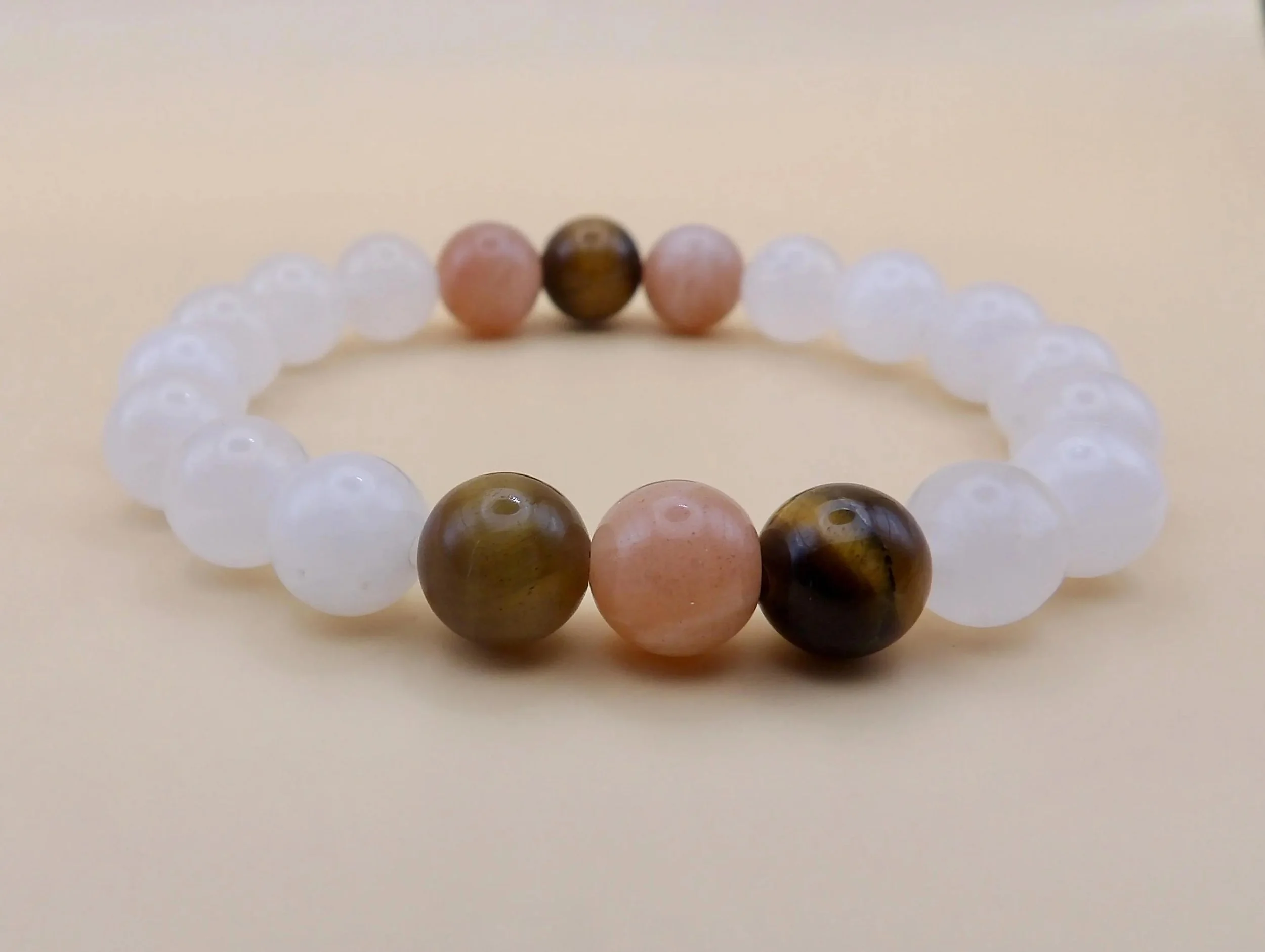 handcrafted warm-neutral gemstone jewelry designed for a comfortable stretch fit, styled on a warm terracotta and beige background.