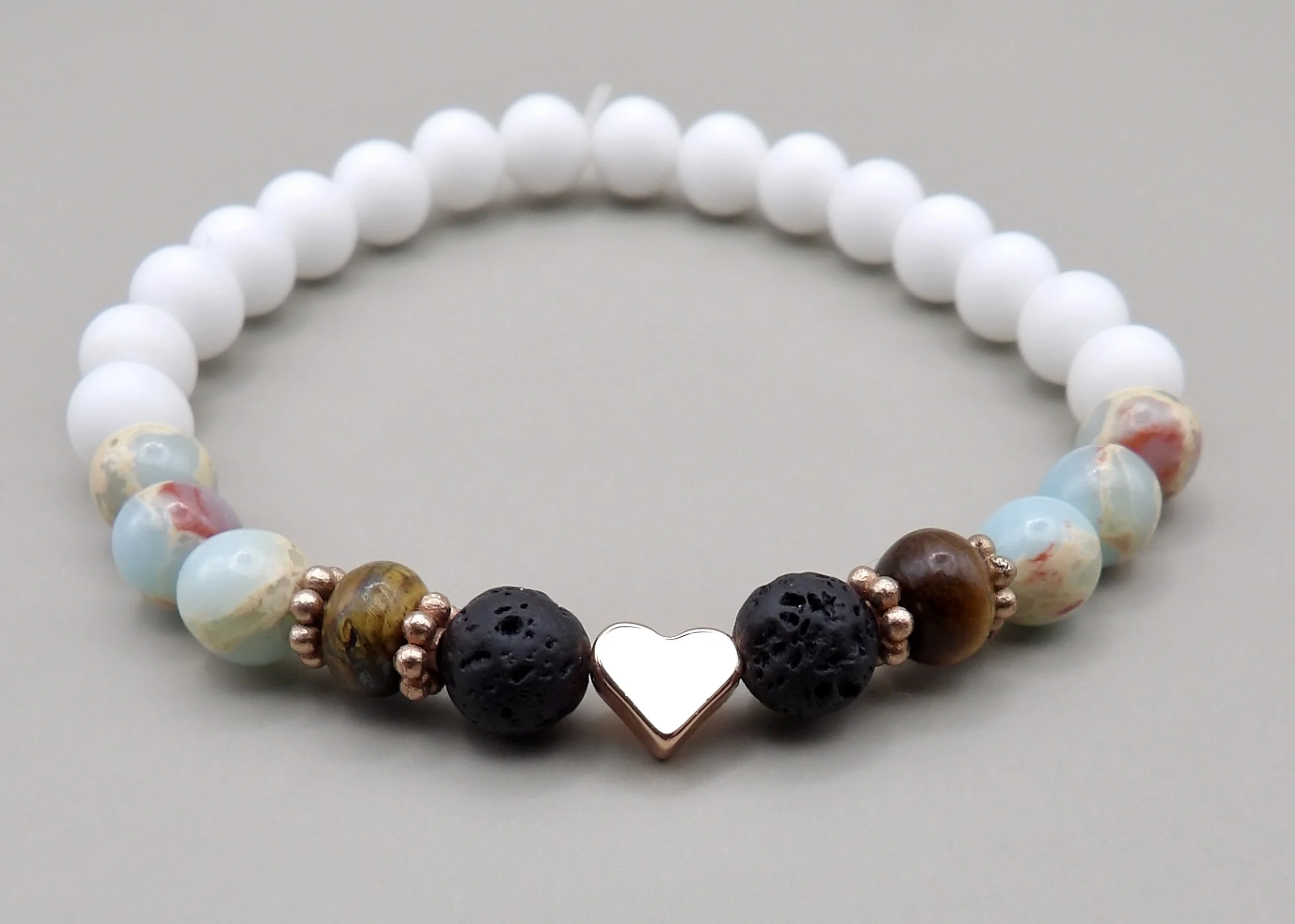 close-up detail of the shiny rose gold heart and daisy spacers flanked by porous lava rock and polished tiger’s eye beads.