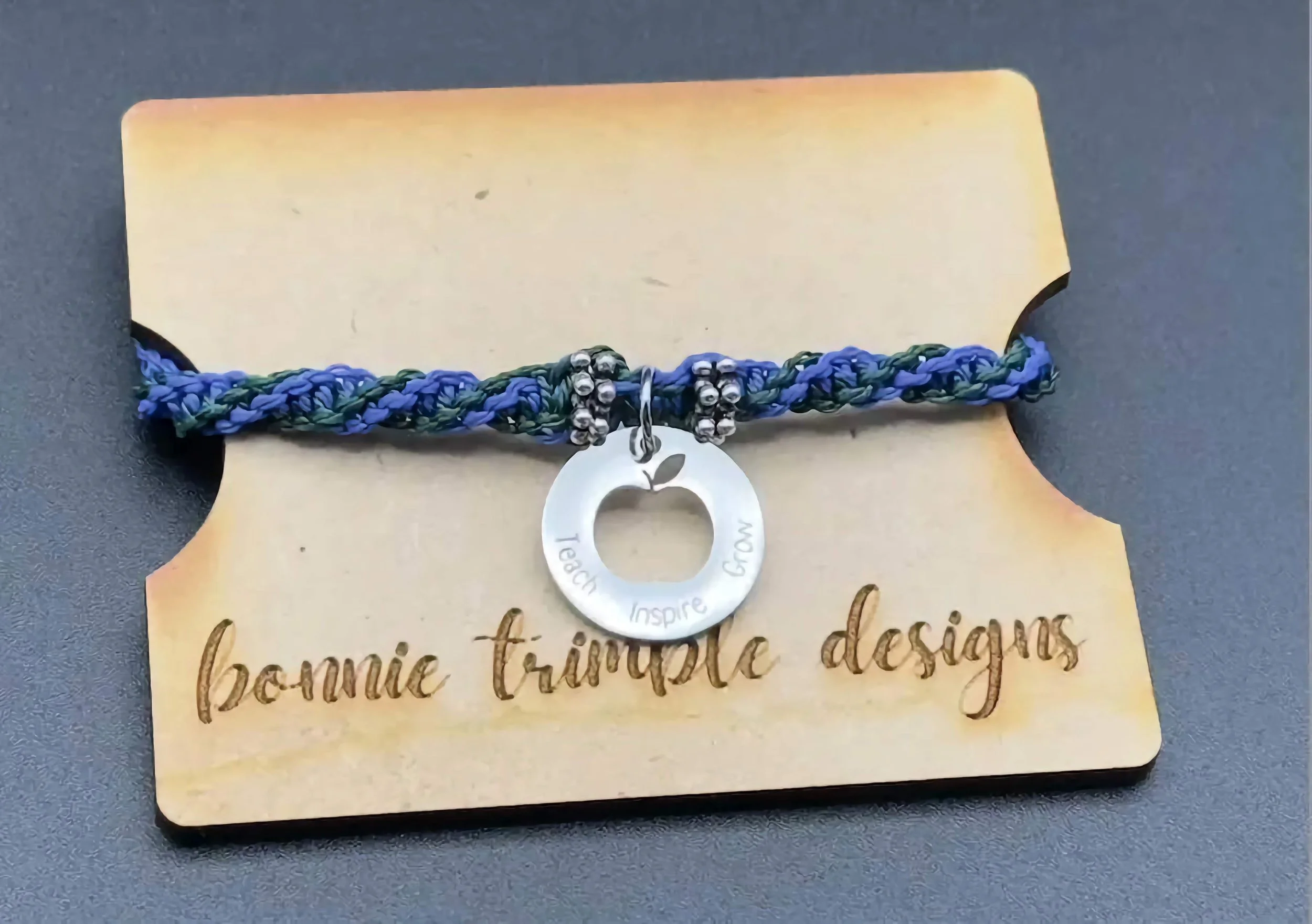 A close-up of a handmade teacher appreciation bracelet featuring a 'teach inspire grow' engraved disc.