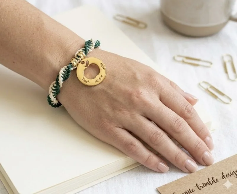 forest green and beige twisted macramé bracelet on a wrist with an 18k gold plated 'teach inspire grow' charm.