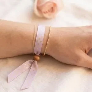 lilac satin ribbon bracelet on a wrist featuring gold polka dots and a wooden toggle clasp.