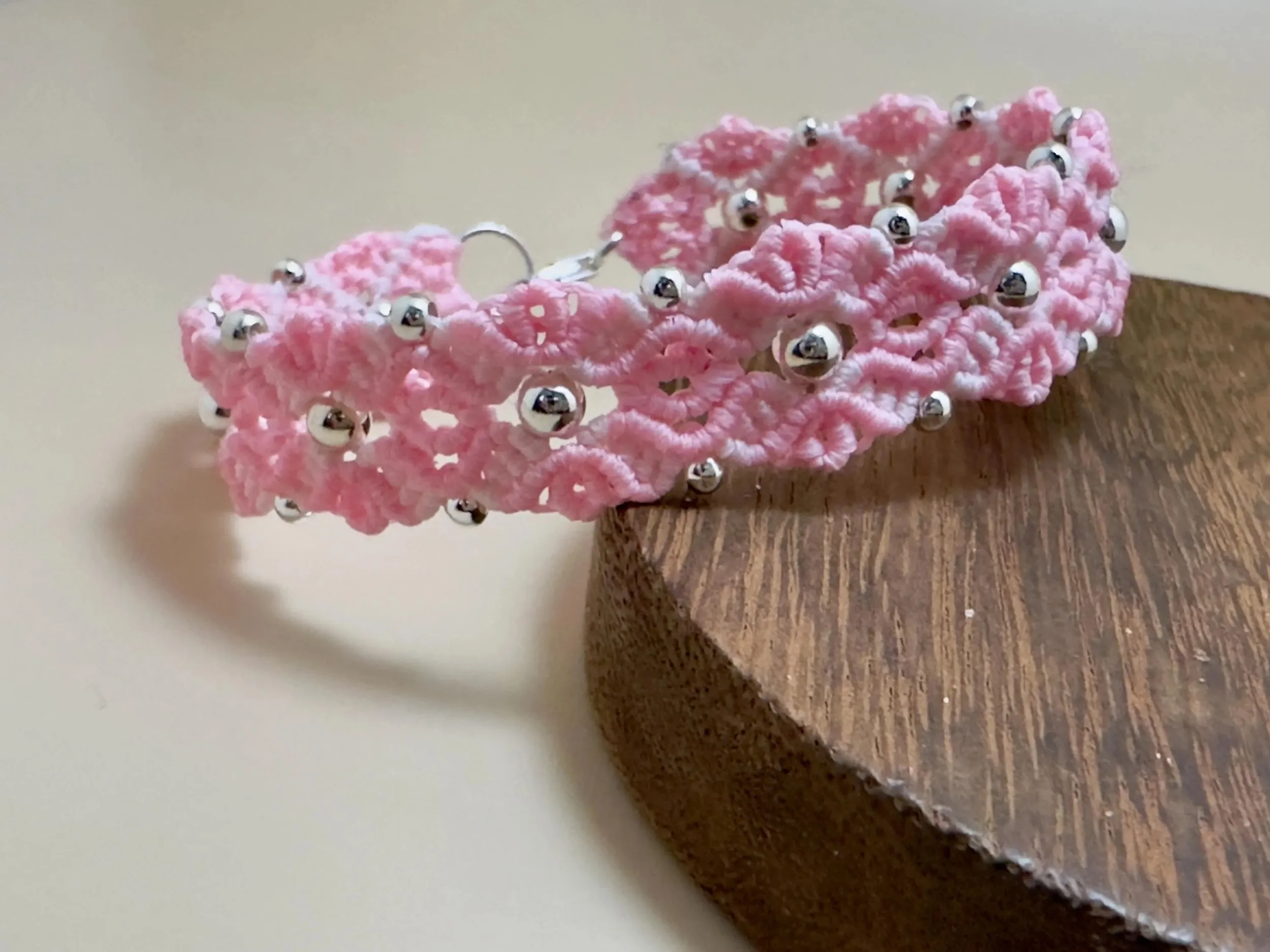 a master-weaver jewelry piece featuring a repeating floral micro-macramé pattern in light pink and sterling silver.