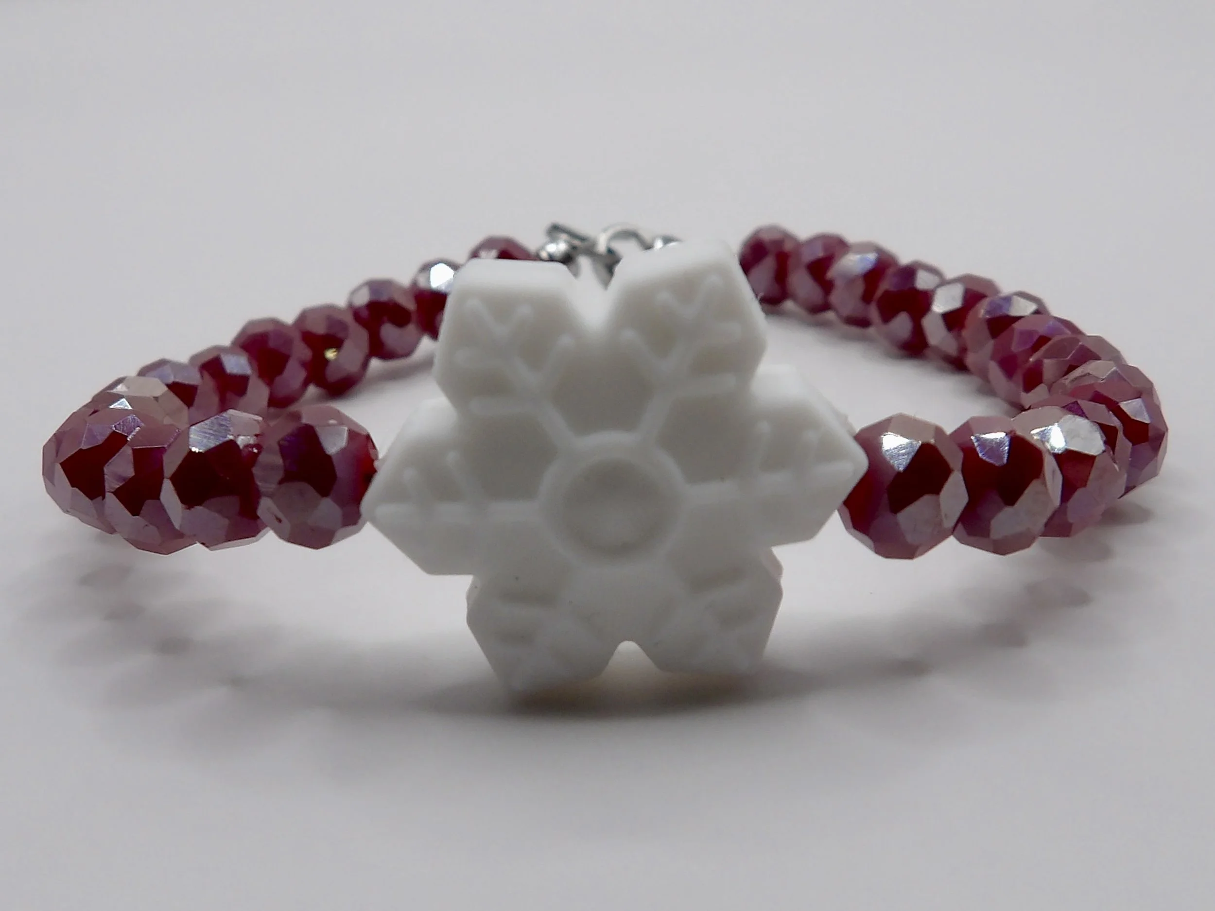 handmade holiday bracelet with deep red faceted glass beads, a white silicone snowflake charm, and stainless steel clasp.