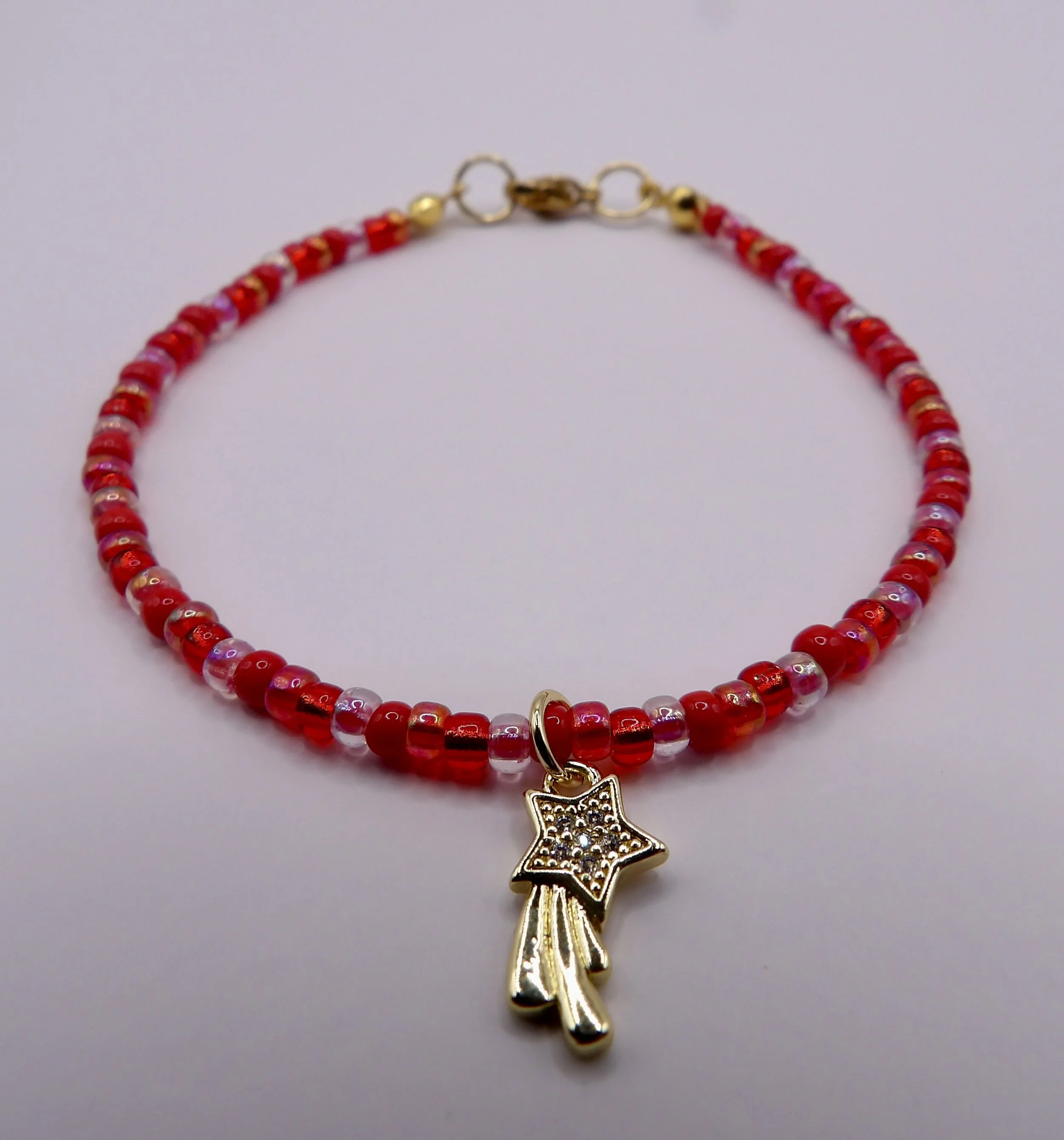 close-up detail of the 18k gold and cz pave shooting star charm on a handmade bracelet with various red seed beads.