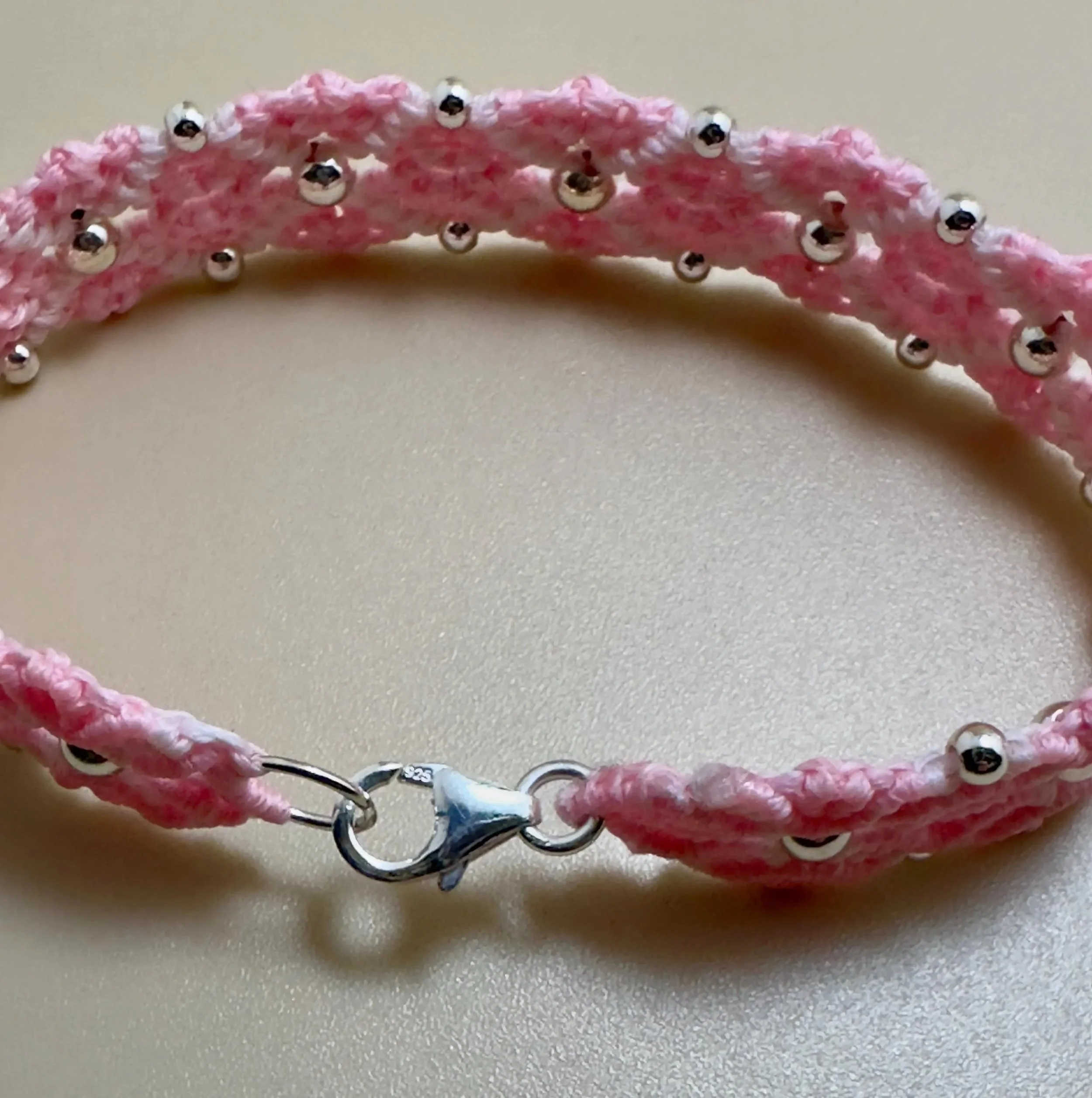 high-resolution editorial shot of the light pink woven bloom bracelet on a soft silk background to show texture.