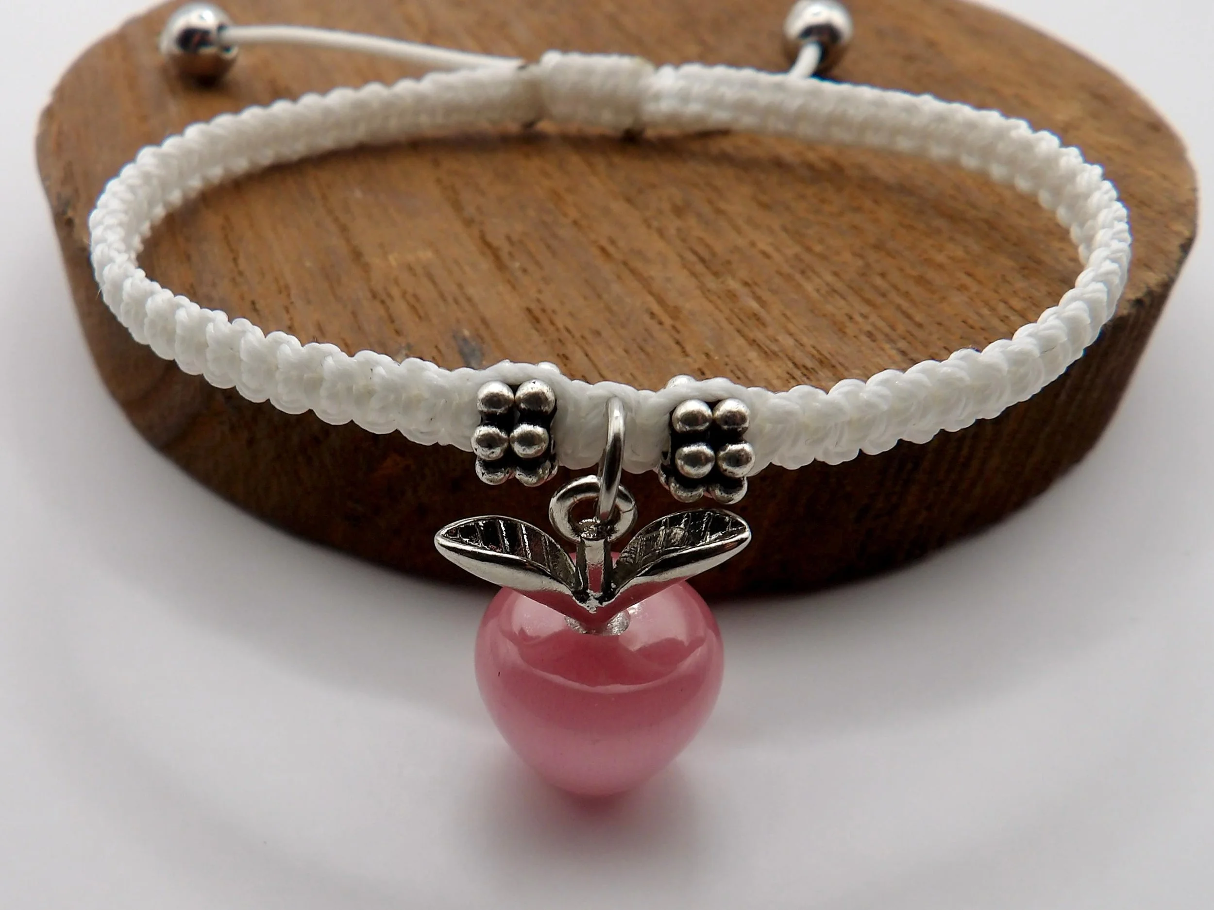 Pink botanical apple charm bracelet showcasing intricate micro-macramé weaving techniques and a soft spring color palette.