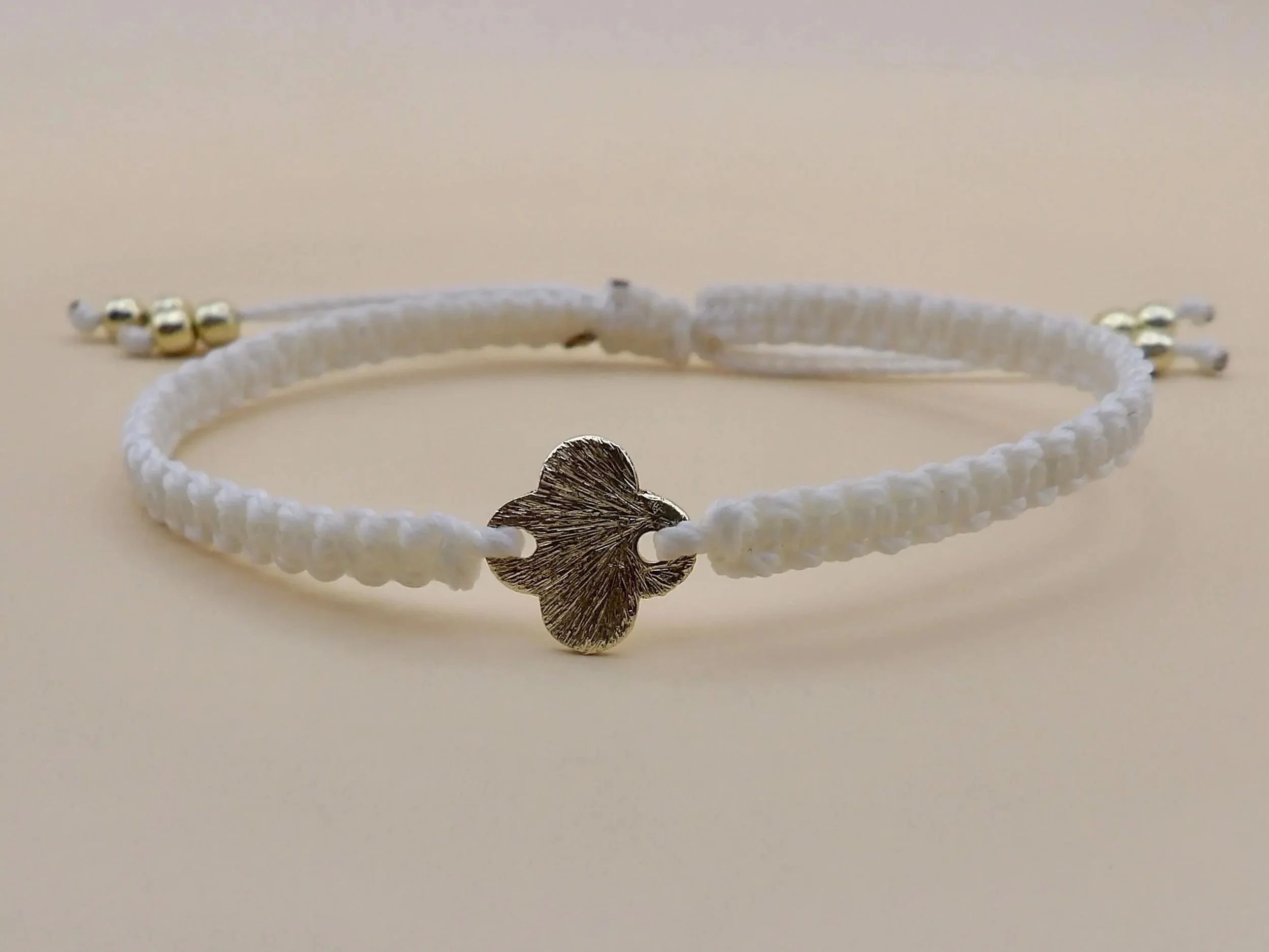 close-up of the quiet faith bracelet highlighting the crisp, uniform knots of the beige fiber wrapping around the gold cross charm.