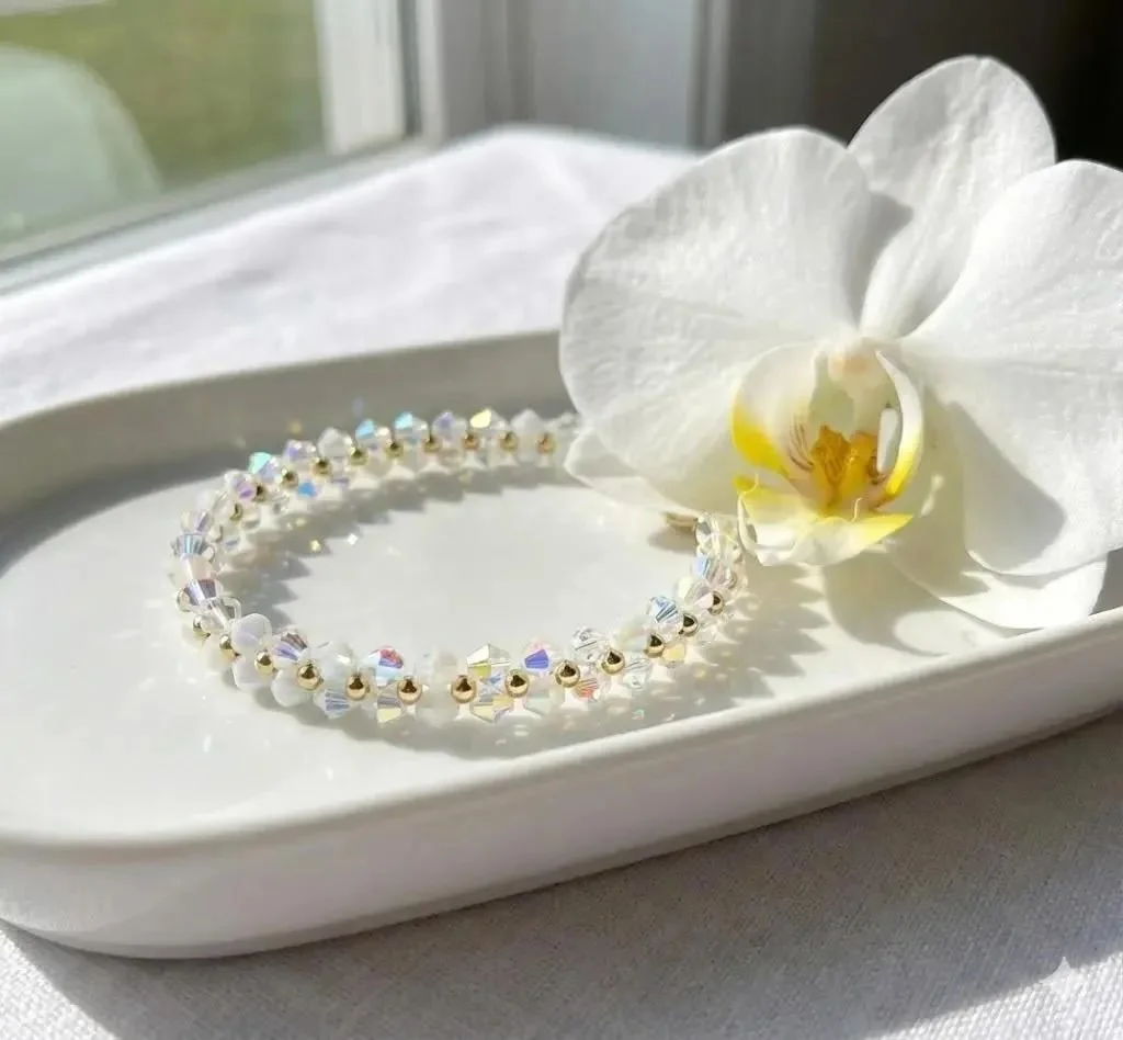 Dainty white crystal daisy chain jewelry with high-shine gold accents, showcasing a delicate and light-catching floral weave.