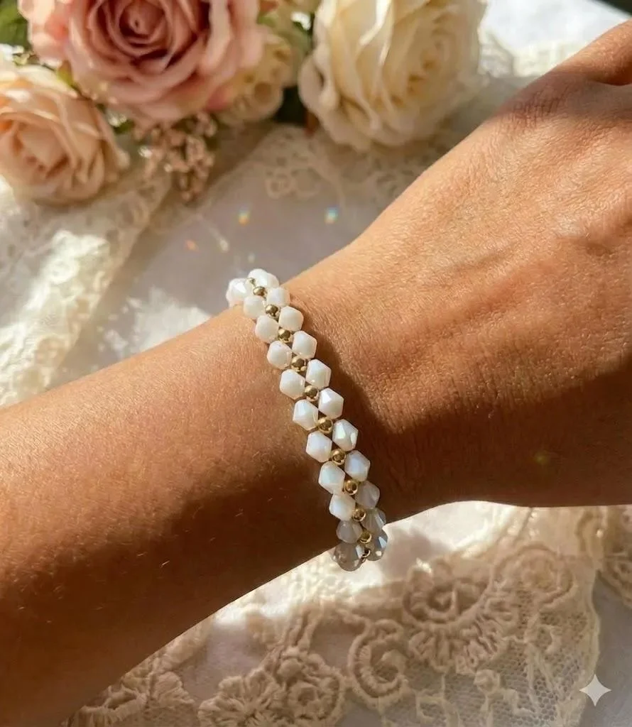 Intricate woven crystal flower bracelet with white bicone petals and polished 18k gold plated bead centers on a soft-focus background.
