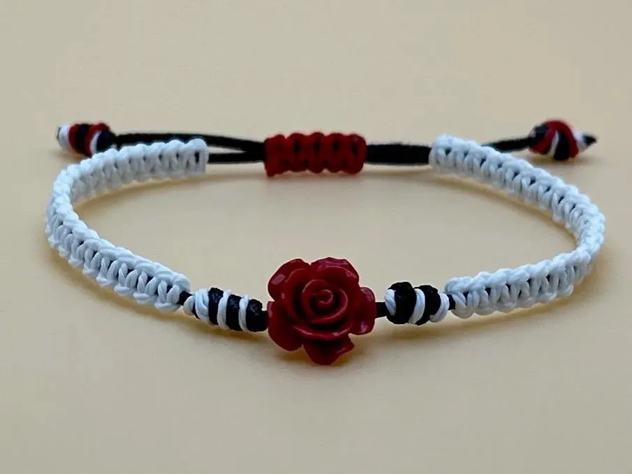 Handmade black and white macrame bracelet featuring dyed red jasper beads and a central, intricately carved rose bead.