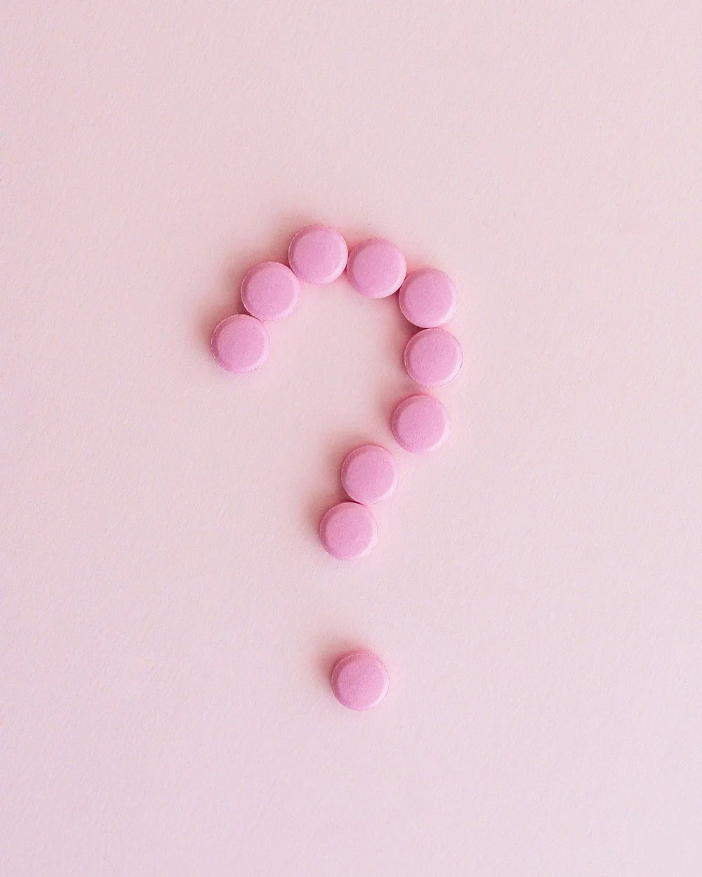 Pink pills on a pink background in a question mark shape