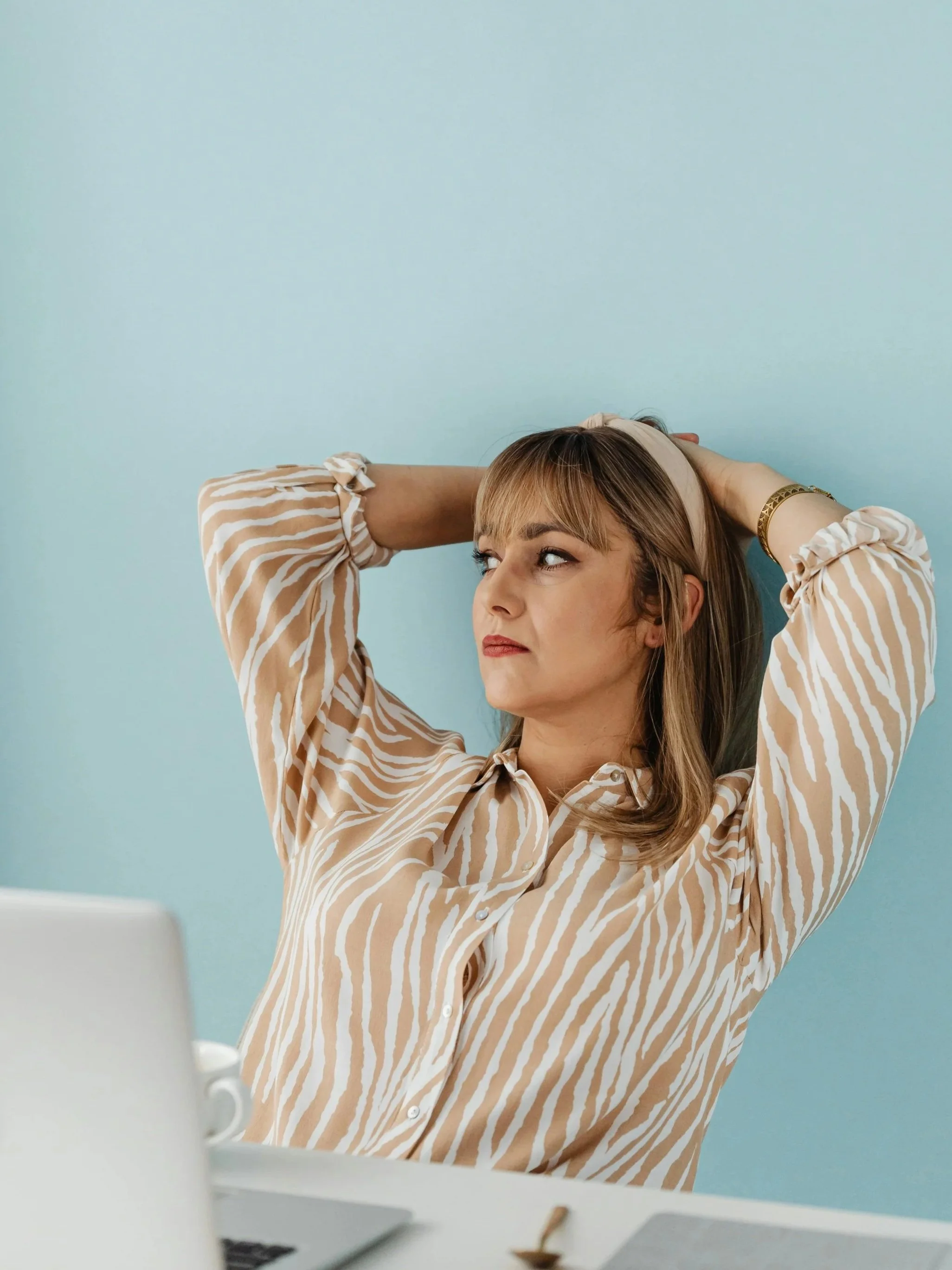 Woman in her early 40s with her arms above her head thinking