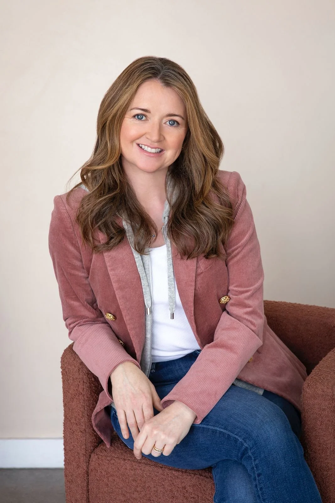 Meghan Rabbitt wearing a pink blazer and sitting in an armchair