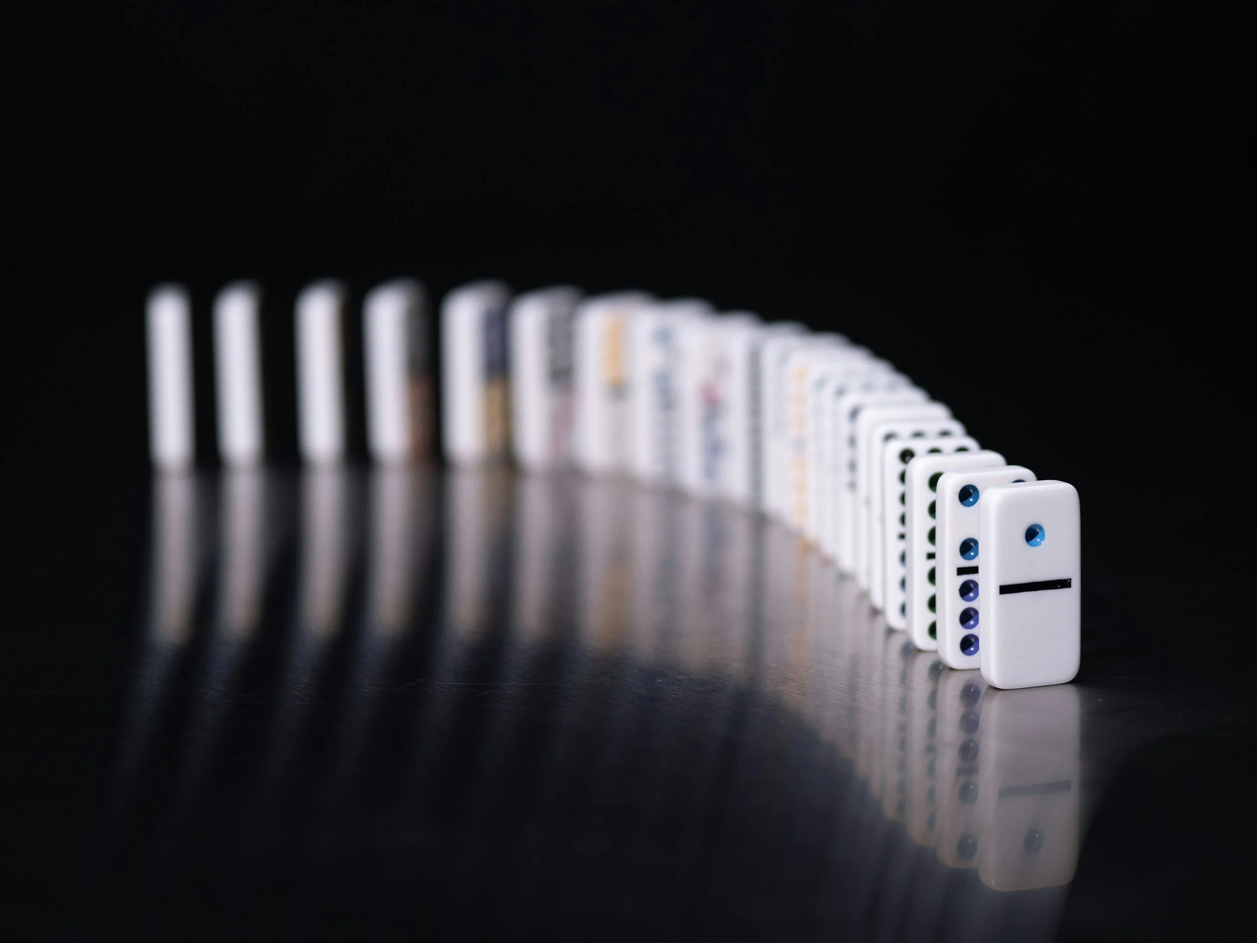 Row of dominos with the first domino knocked over against a black background, creating a domino effect.