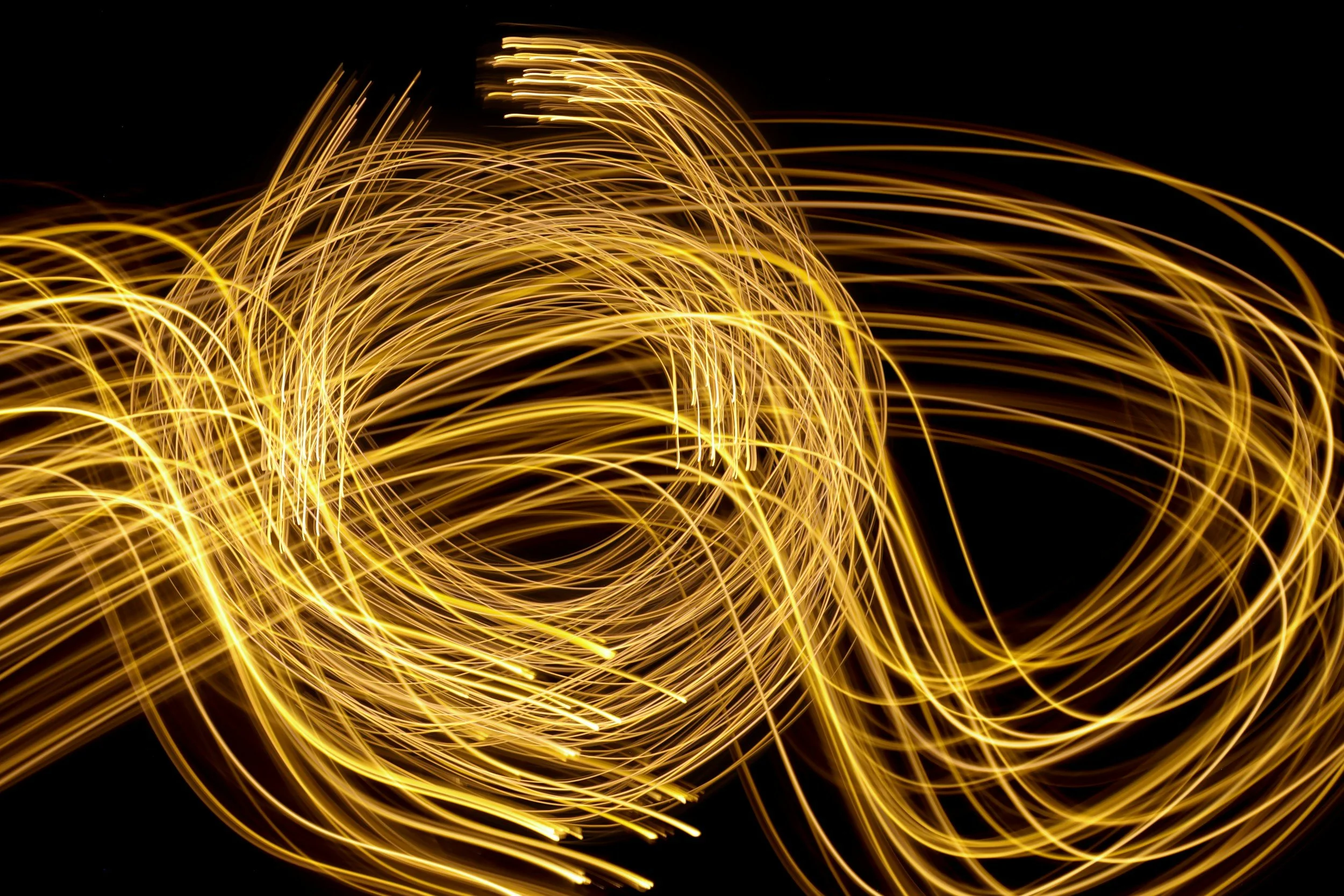 Long exposure photograph of swirling golden light trails against a black background.