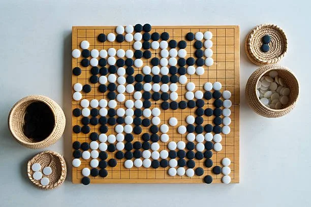 An overhead view of a Go board with black and white stones, surrounded by baskets holding extra stones.