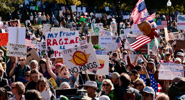 Crowd of people protesting outdoors, holding signs and American flags.