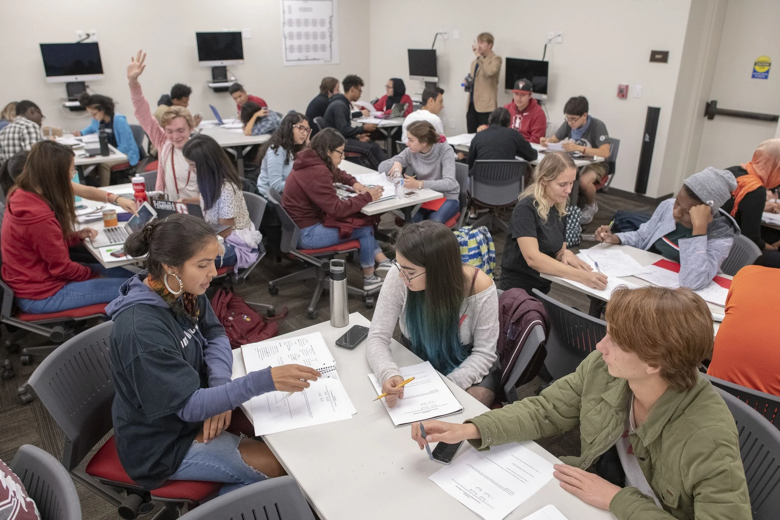 College classroom with students working and a teacher standing at the front.