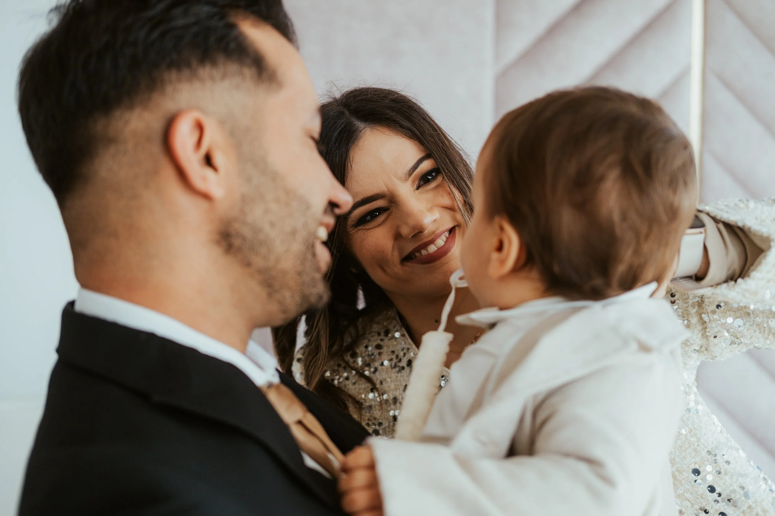 Família sorridente incluindo um homem, uma mulher e uma criança, interagindo alegremente em um ambiente interno.