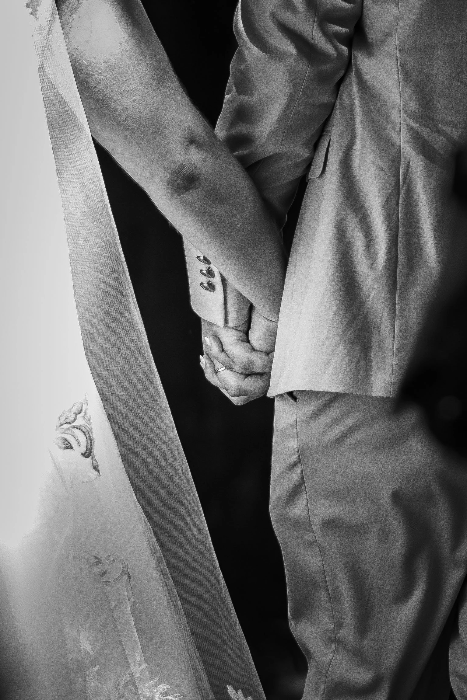 Imagem em preto e branco de duas pessoas segurando as mãos, uma vestindo terno e a outra com uma manga curta. O foco é nas mãos entrelaçadas.