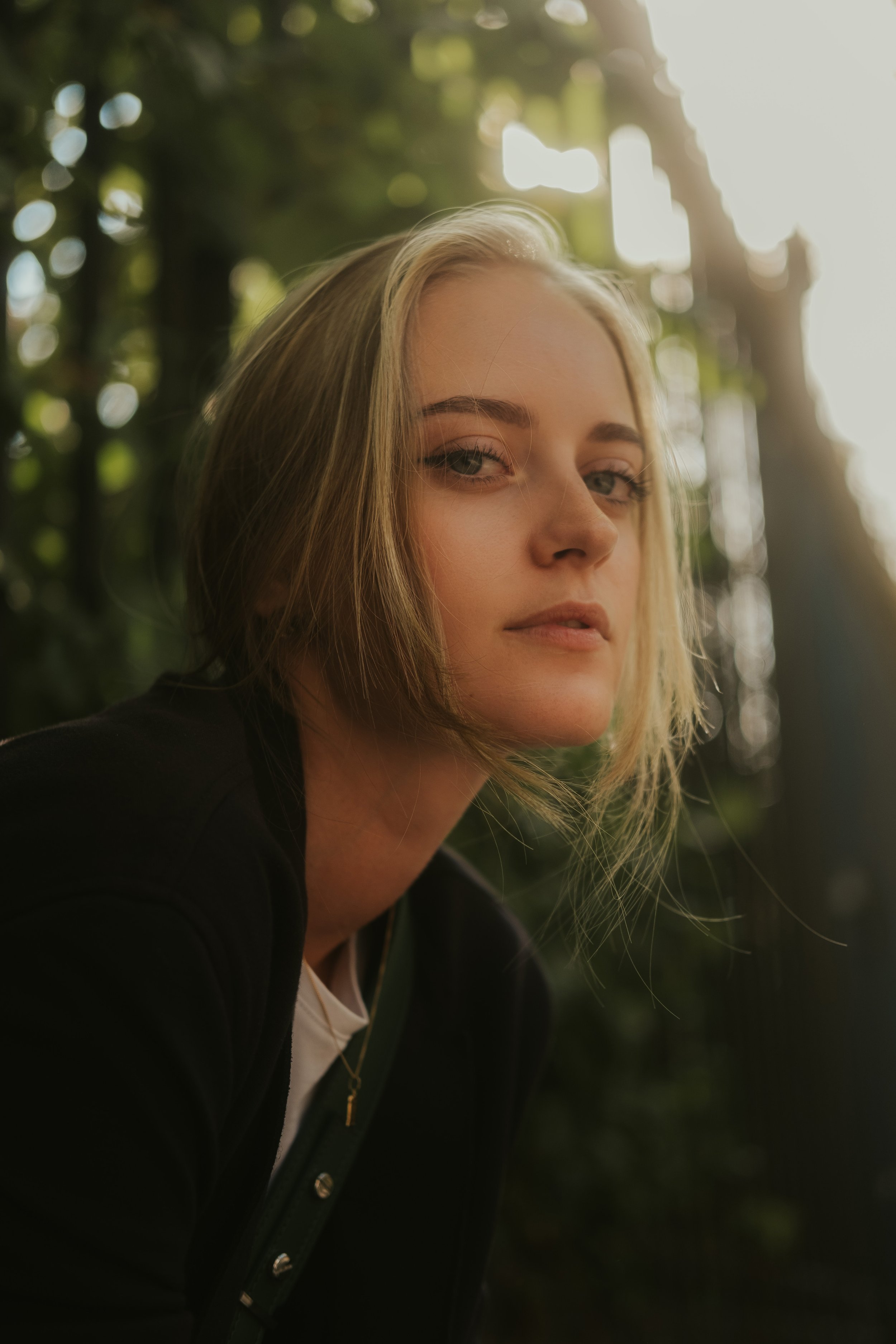 Retrato de uma mulher com cabelo loiro, de pele clara, olhando de lado com expressão séria, ao ar livre com iluminação natural.