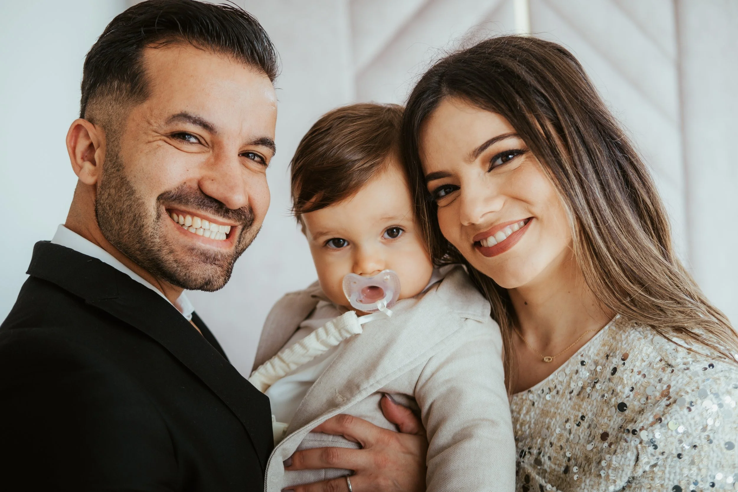 Família sorridente com pai, mãe e filho em close-up, em ambiente interno bem iluminado.