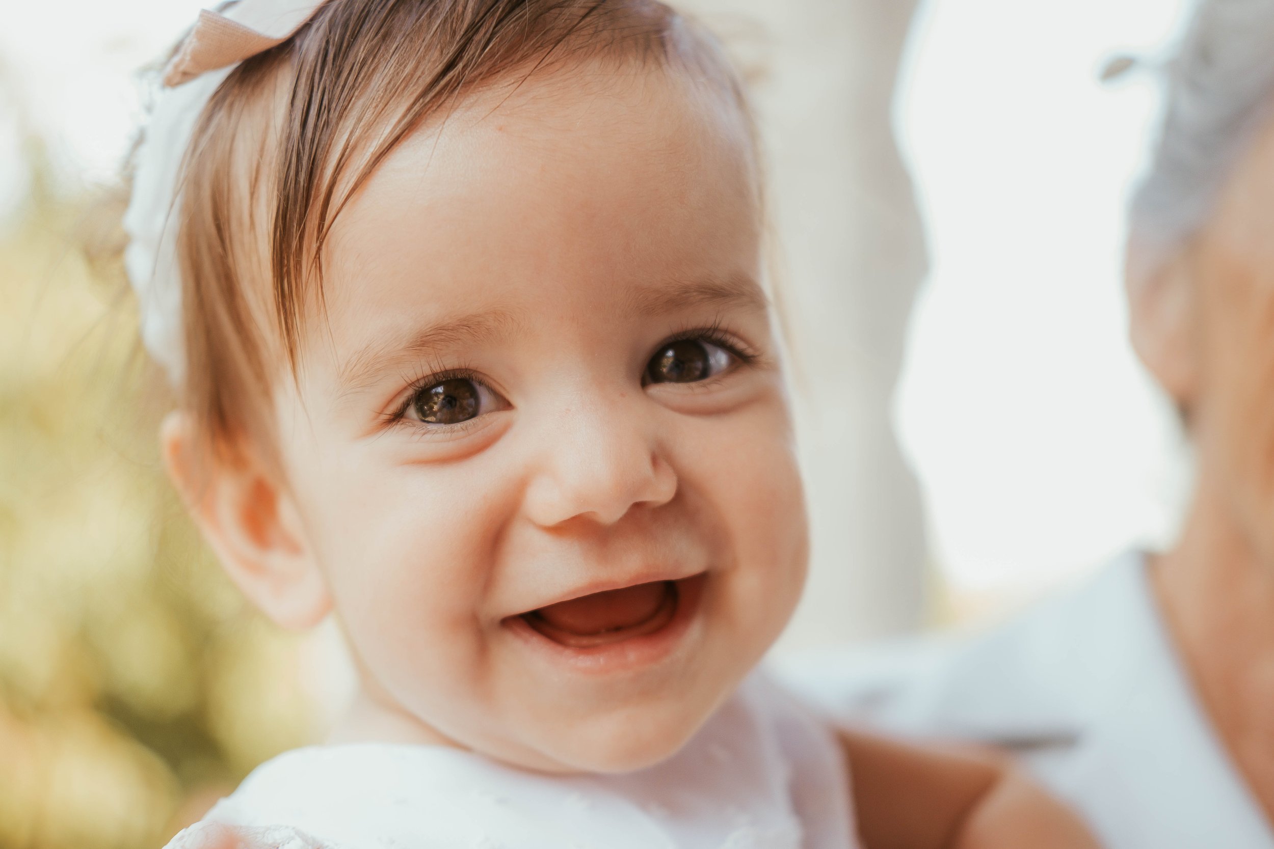 Retrato de uma criança sorridente com cabelos castanhos e olhos claros, usando uma fita branca na cabeça, em um ambiente com iluminação natural.