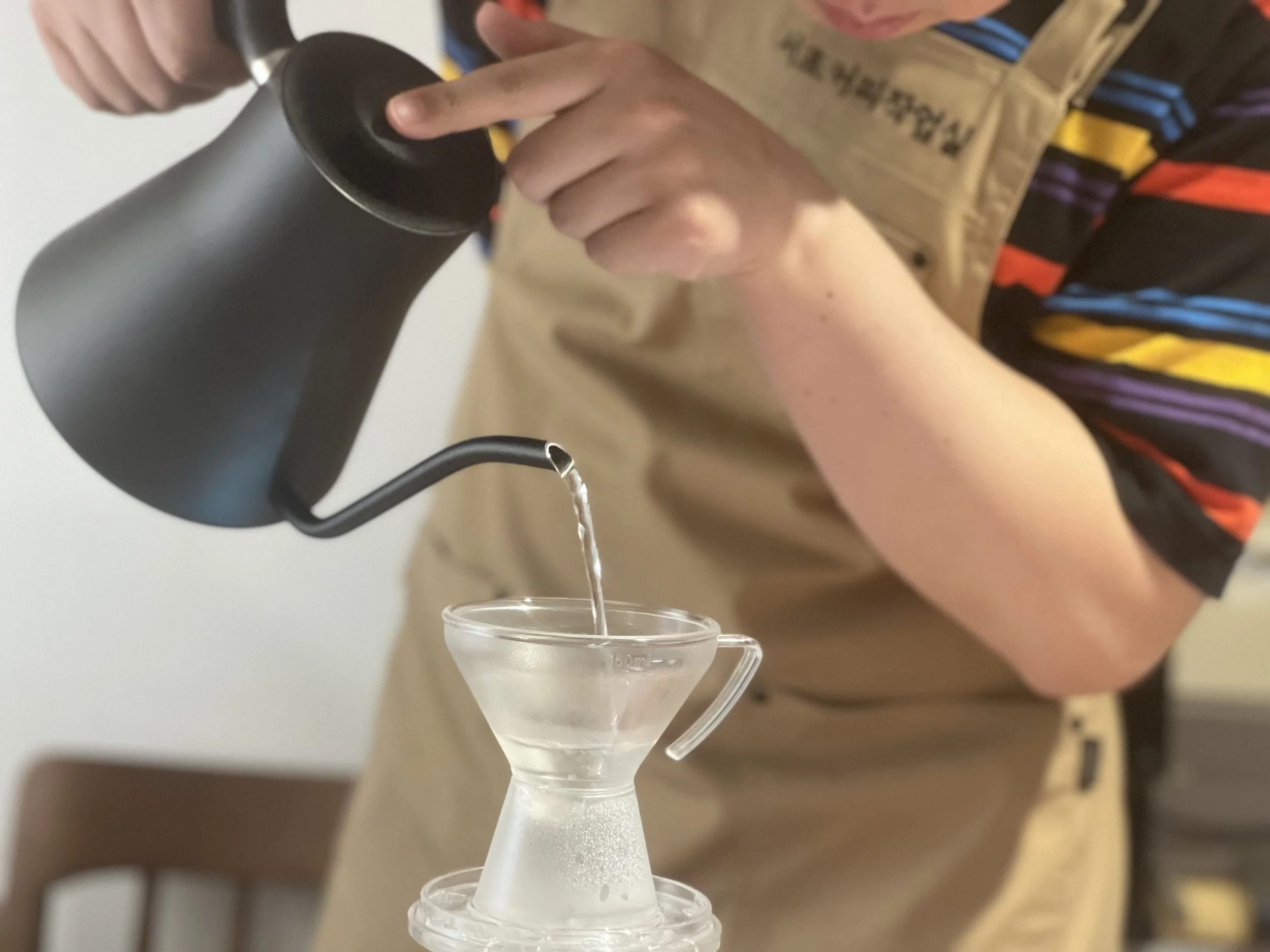 Person pouring water from a black kettle into a glass coffee brewing vessel.