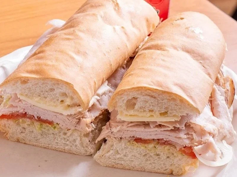 Two submarine sandwiches with turkey, lettuce, tomato, and mayonnaise on white bread, placed on a plate.
