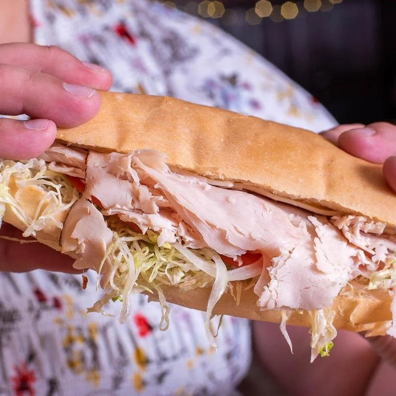 Close-up of a person holding a sandwich with sliced turkey, shredded lettuce, and a hoagie roll.