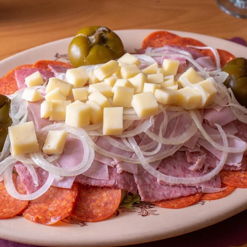 Plate of sliced pepperoni, ham, chopped onions, green olives, and shredded cheese.