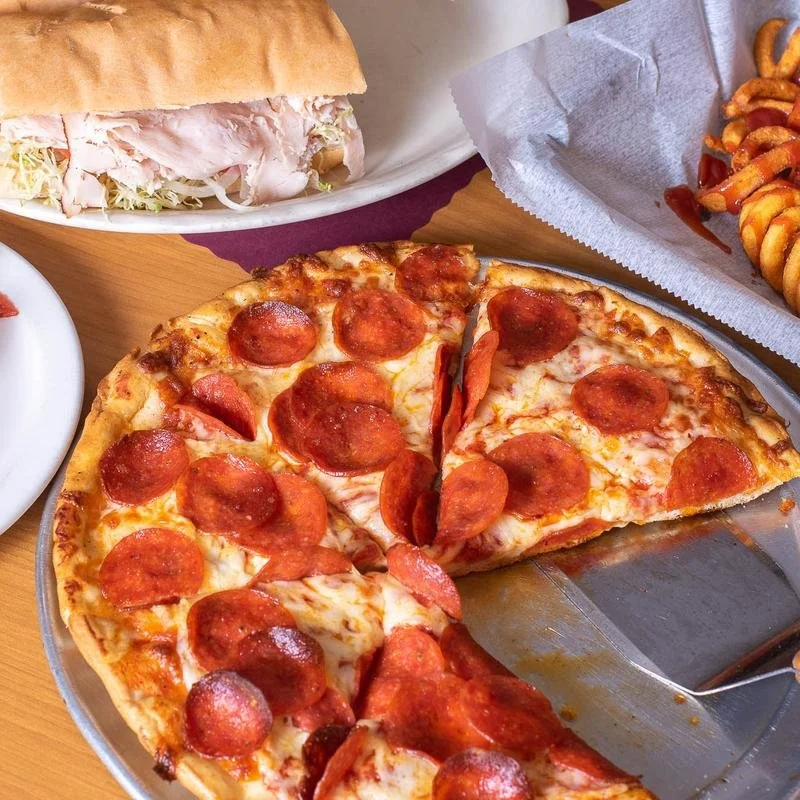 A slice of pepperoni pizza on a metal tray, with part of the pizza missing, cheese, and pepperoni toppings.