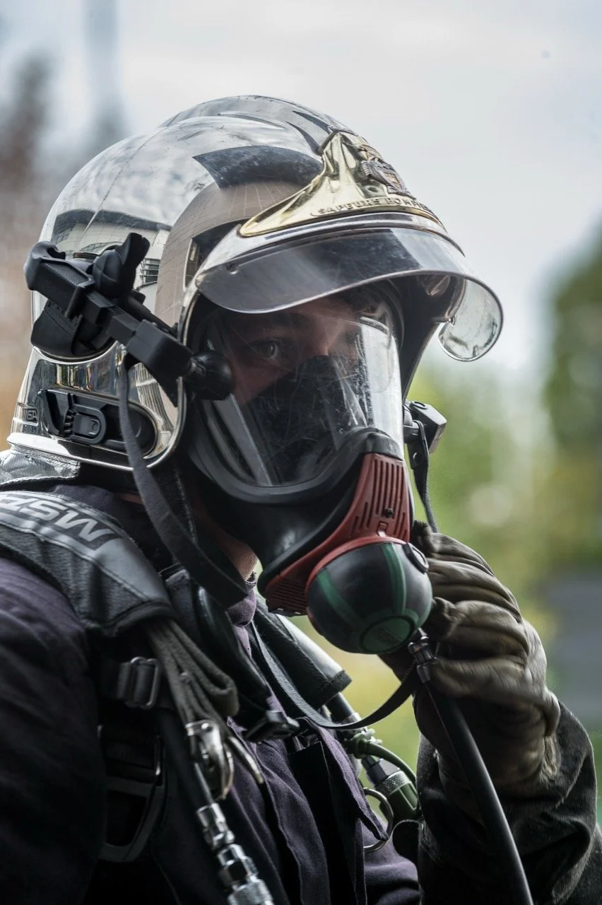 Pompier en tenue d’intervention portant un casque argenté et un masque respiratoire ARI avec visière.