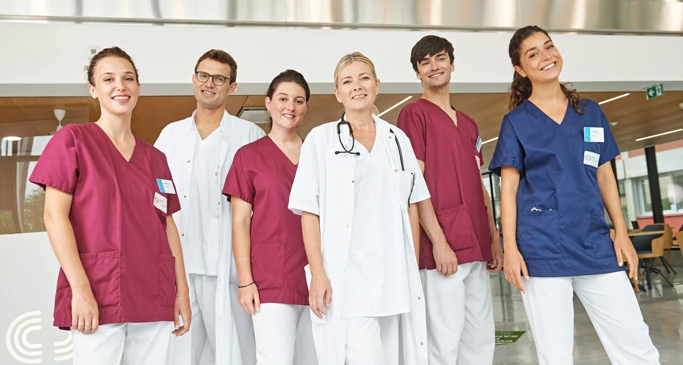 Équipe médicale de six professionnels souriants portant des tenues de soins dans un établissement de santé