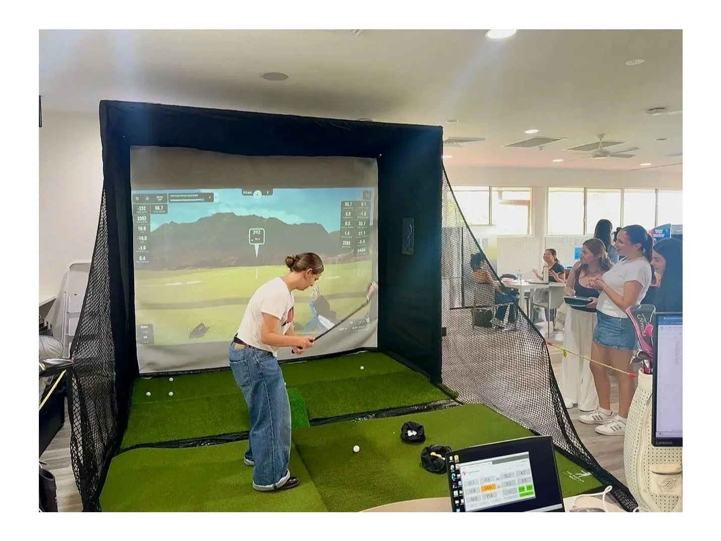 Girl using mobile golf simulator as spectators watch the hit.