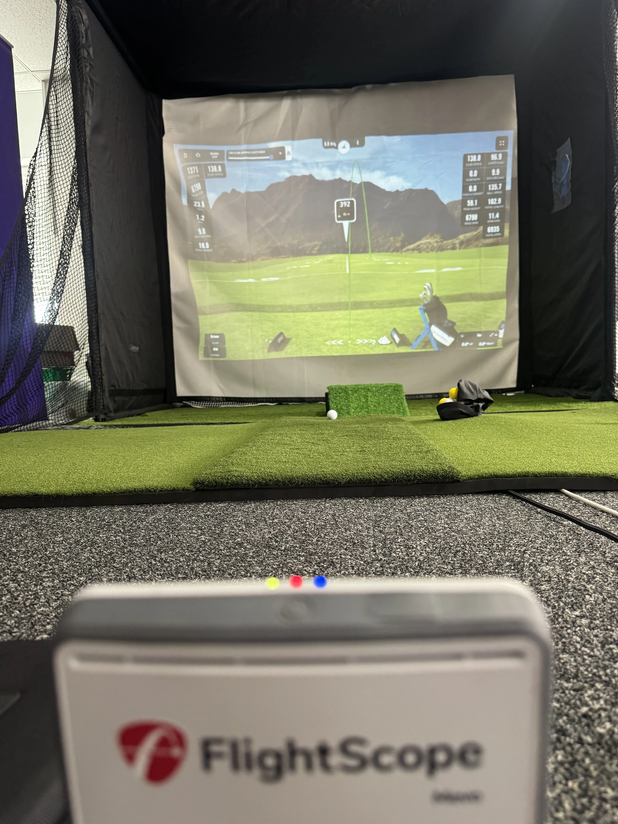 FlightScope Mevo Gen 2 golf simulator setup showing impact screen, hitting mat and Mevo positioned behind the bal.