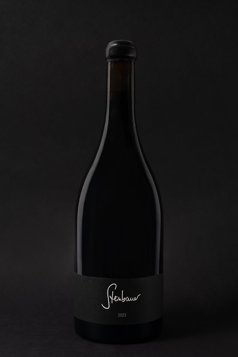 Schwarze Weinflasche auf schwarzem Hintergrund mit minimalistischer Etikette, die den Namen 'Steinbauer' und das Jahr 2023 zeigt.