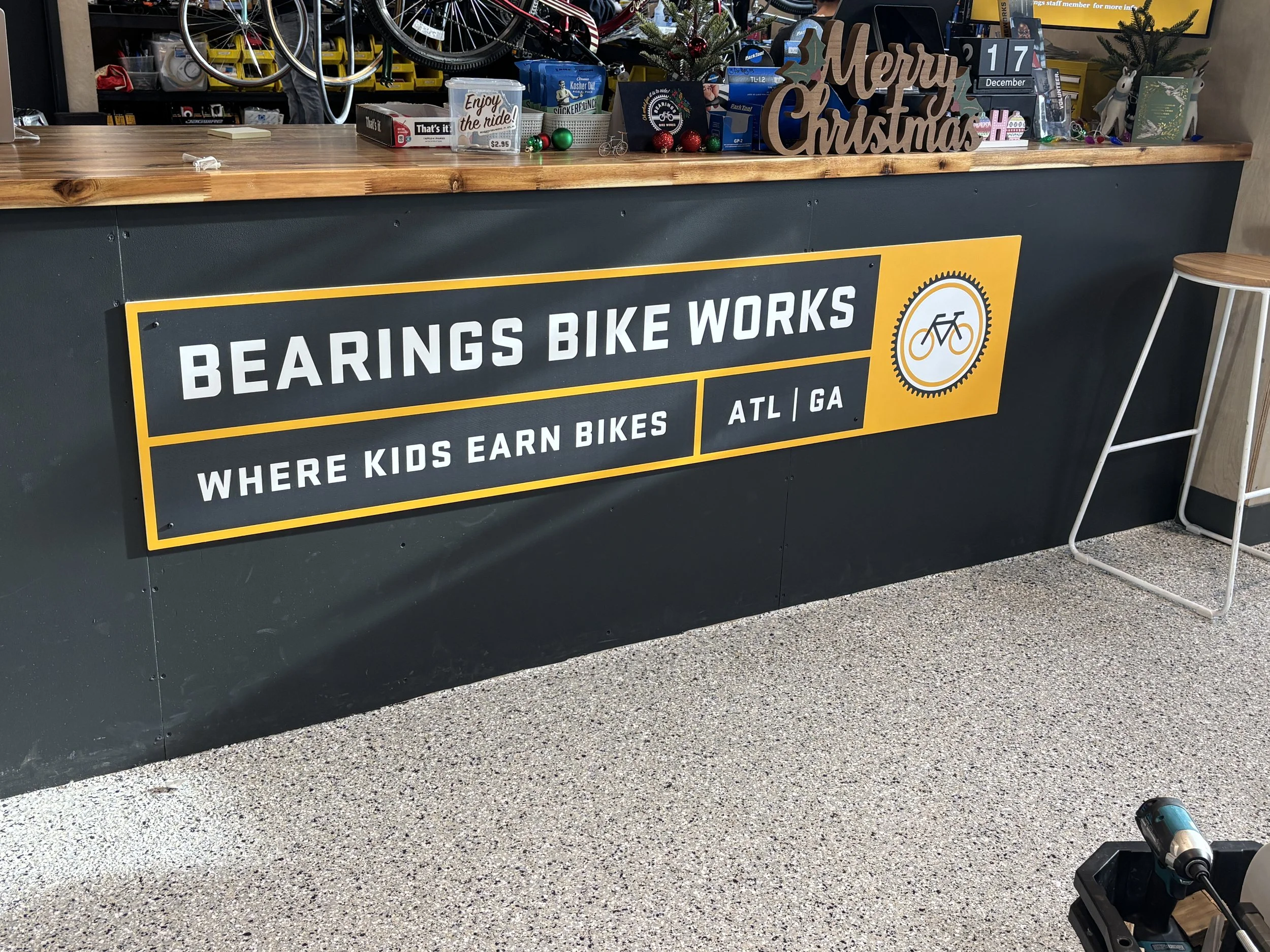 Signboard reading 'Bearings Bike Works' with subtitle 'Where Kids Earn Bikes' and location 'ATL / GA', featuring a bicycle gear and bike icon.