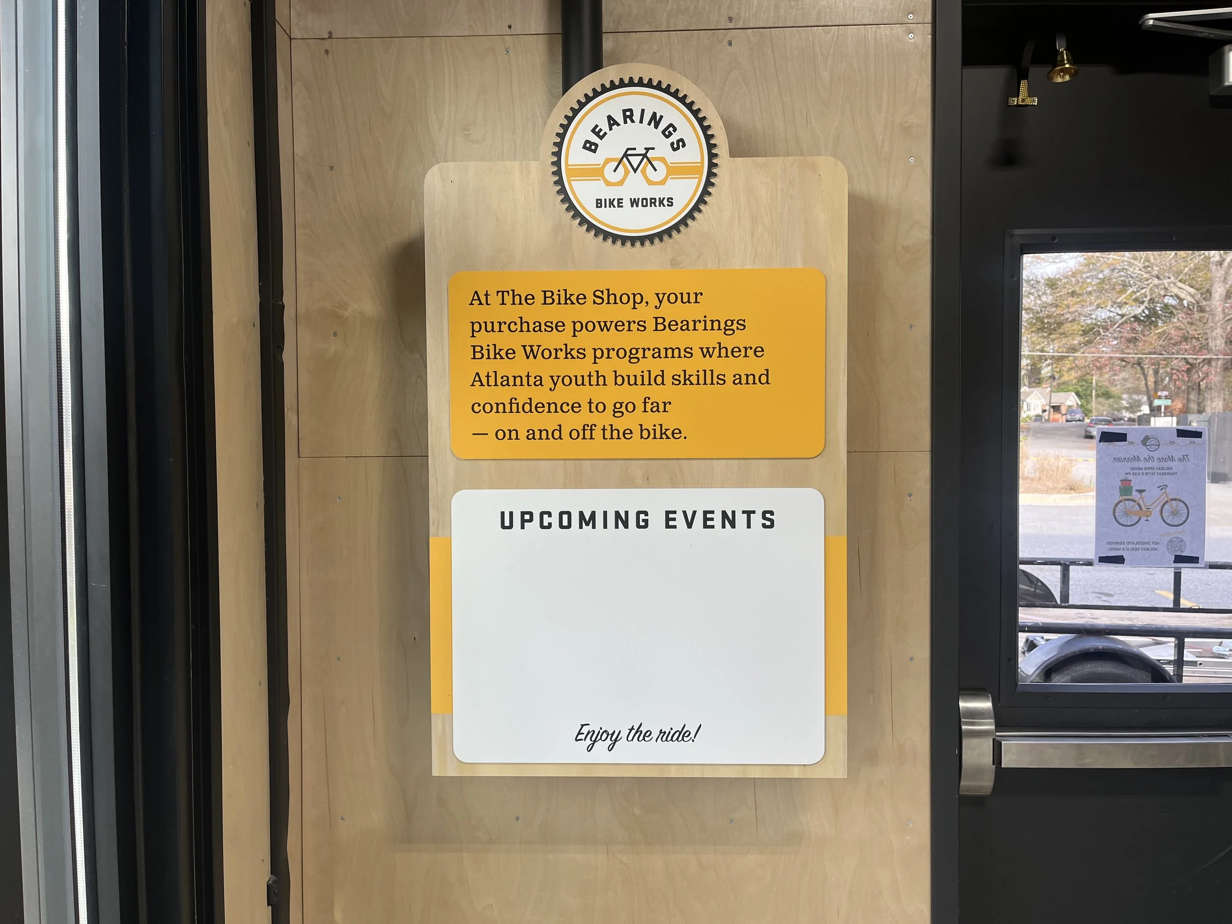 Sign at a bike shop with the logo 'Bearing's Bike Works', includes a yellow section about Atlanta youth building skills and confidence, and a white section for upcoming events with the phrase 'Enjoy the ride!'