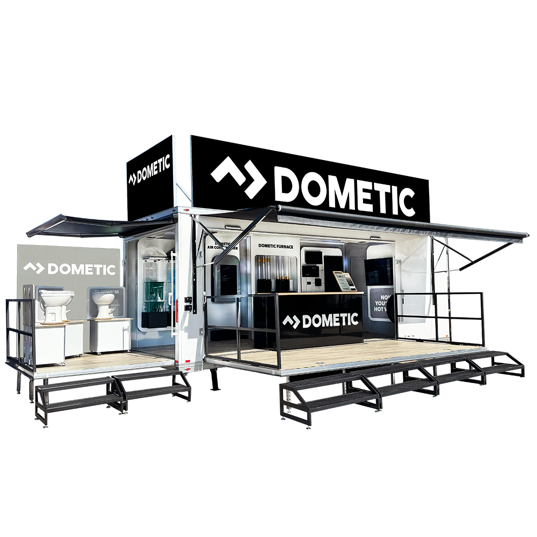 A mobile display trailer with Dometic branding, featuring appliances like toilets, outdoor equipment, and a service counter under black and white branding signs.