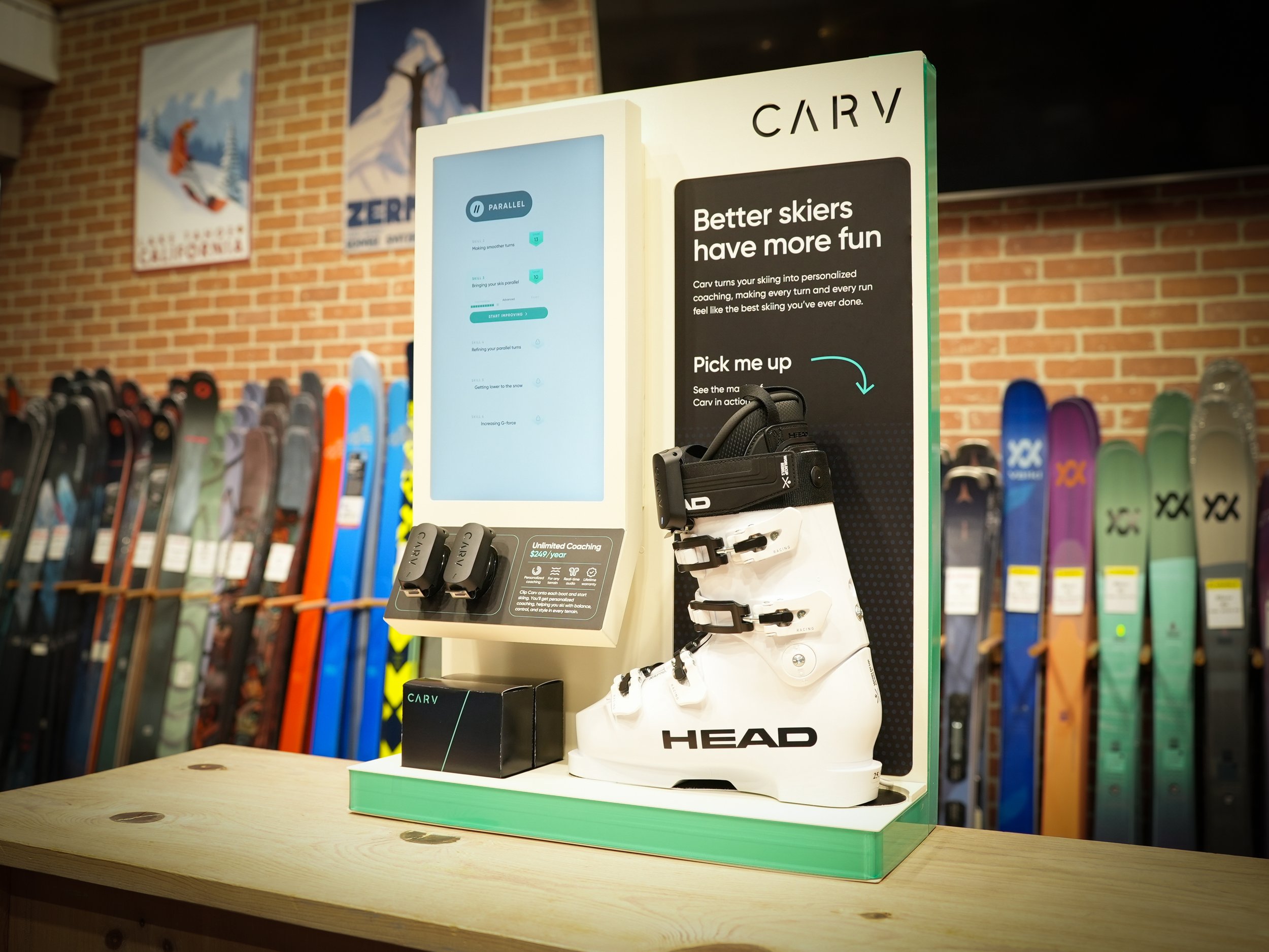 A ski equipment display featuring a promotion for Carv ski coaching. The display includes a large ski boot with bindings, a screen showing coaching information, and various ski boots on shelves in the background.
